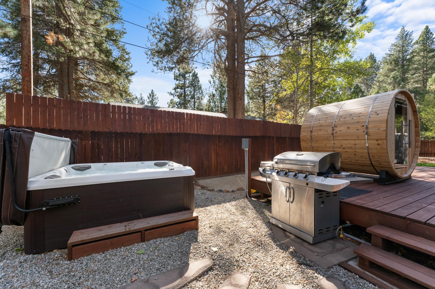 Outdoor area at a Truckee vacation rental featuring a hot tub, barrel sauna, and grill, surrounded by trees.