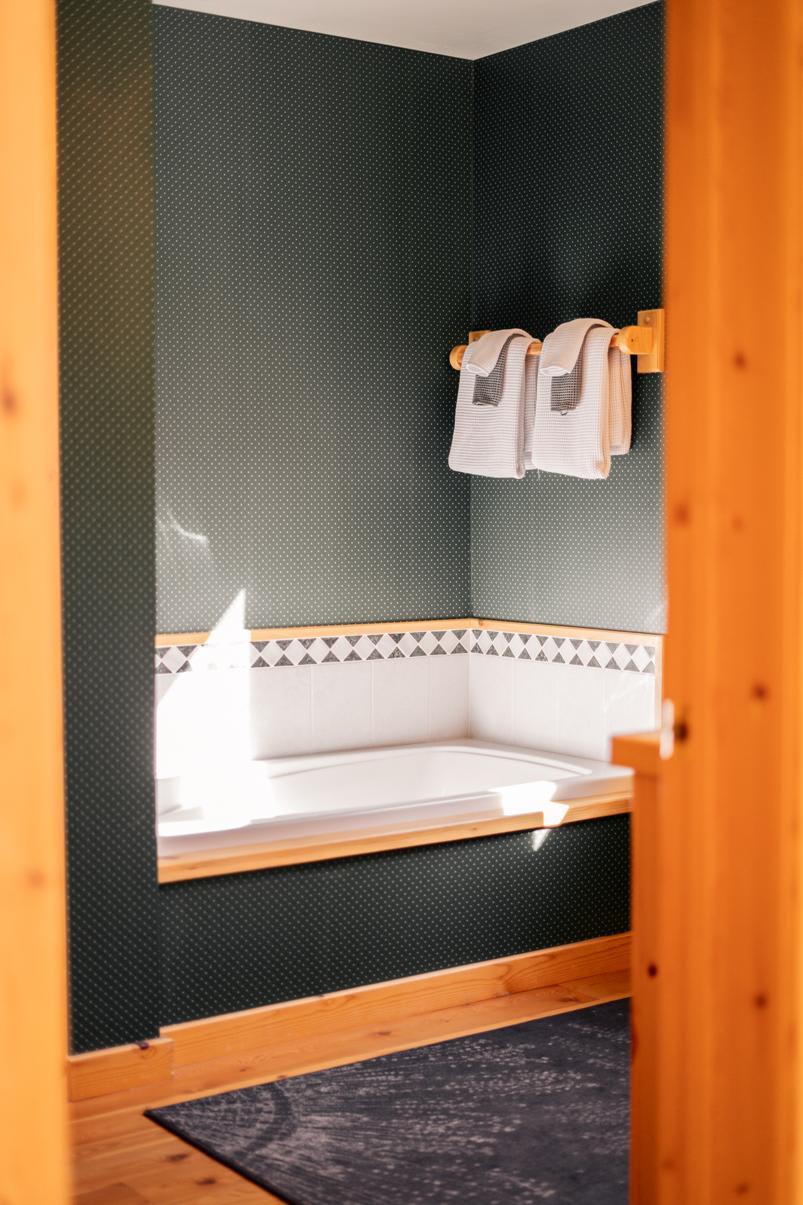 Bathroom in a Truckee vacation rental with green walls, a white tub, and towels on a wooden rack.