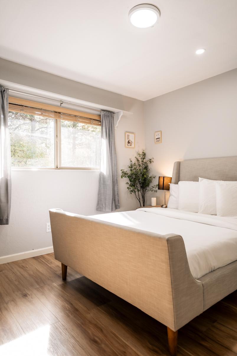 Bright bedroom in a Truckee vacation rental featuring a cozy bed, soft lighting, wooden floors, and a scenic window view.