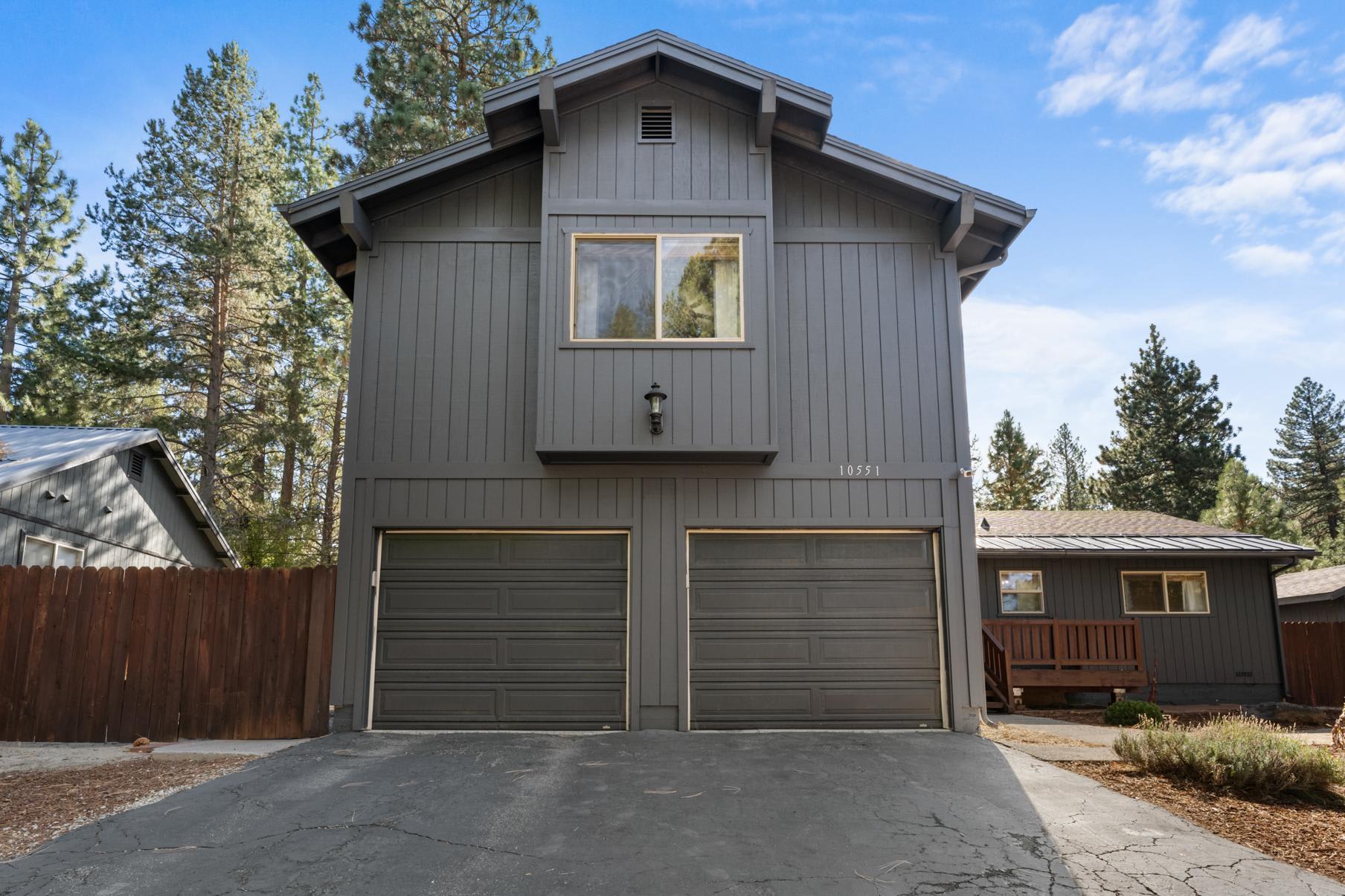 Gray house in Truckee with two-car garage, surrounded by pine trees. Ideal vacation rental for a serene getaway.