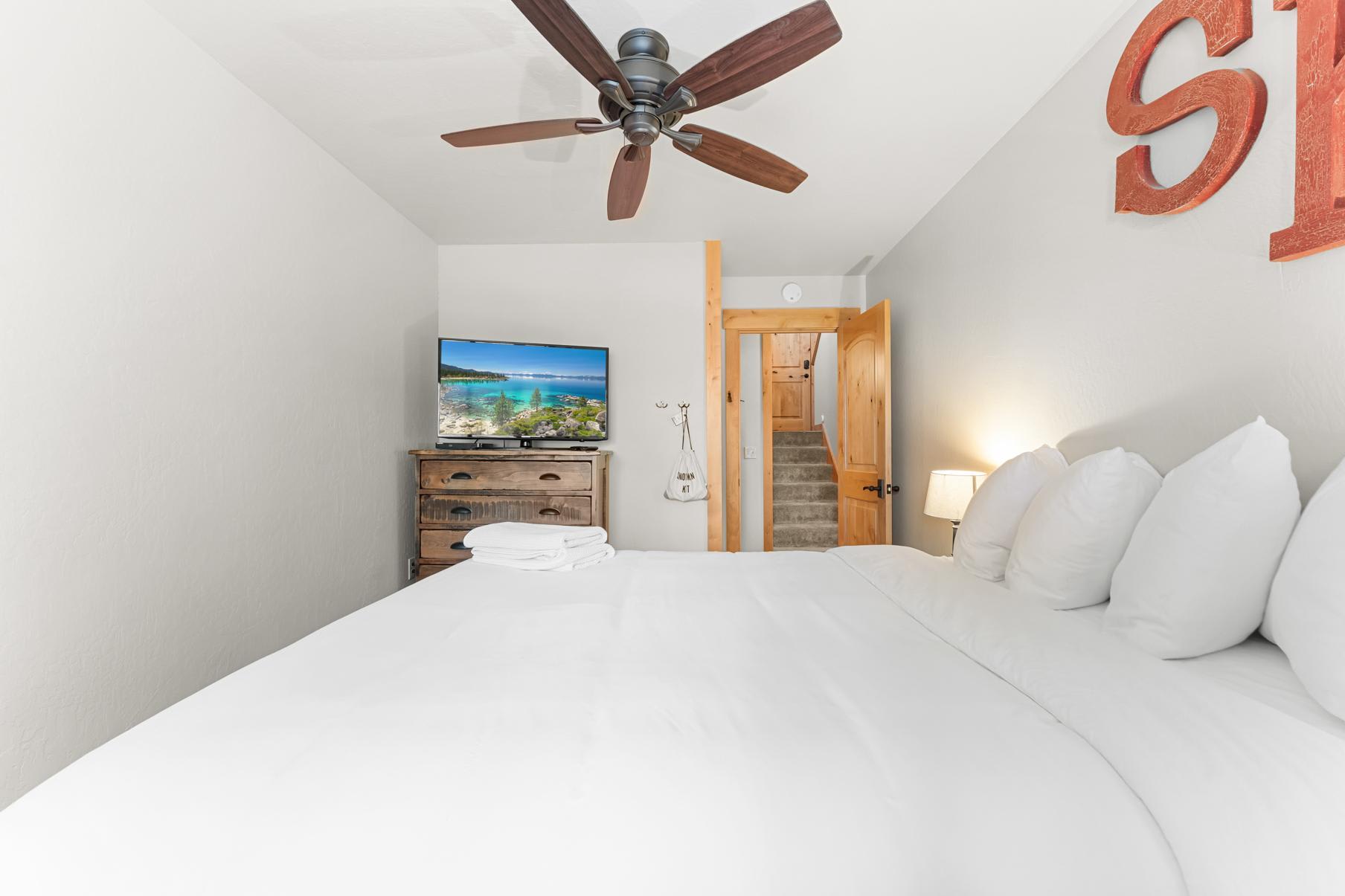 Bedroom in a Truckee vacation rental, featuring a cozy bed, TV on a dresser, and a wooden door leading to stairs.