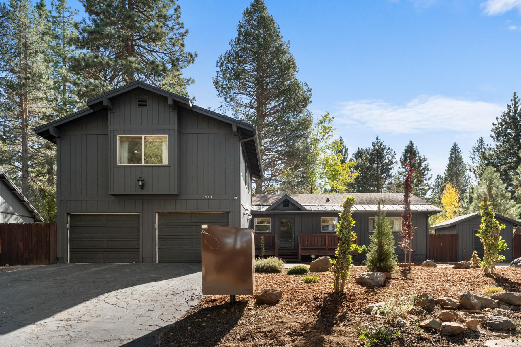 Gray house surrounded by trees, located in Truckee, featured as a vacation rental with a spacious driveway.