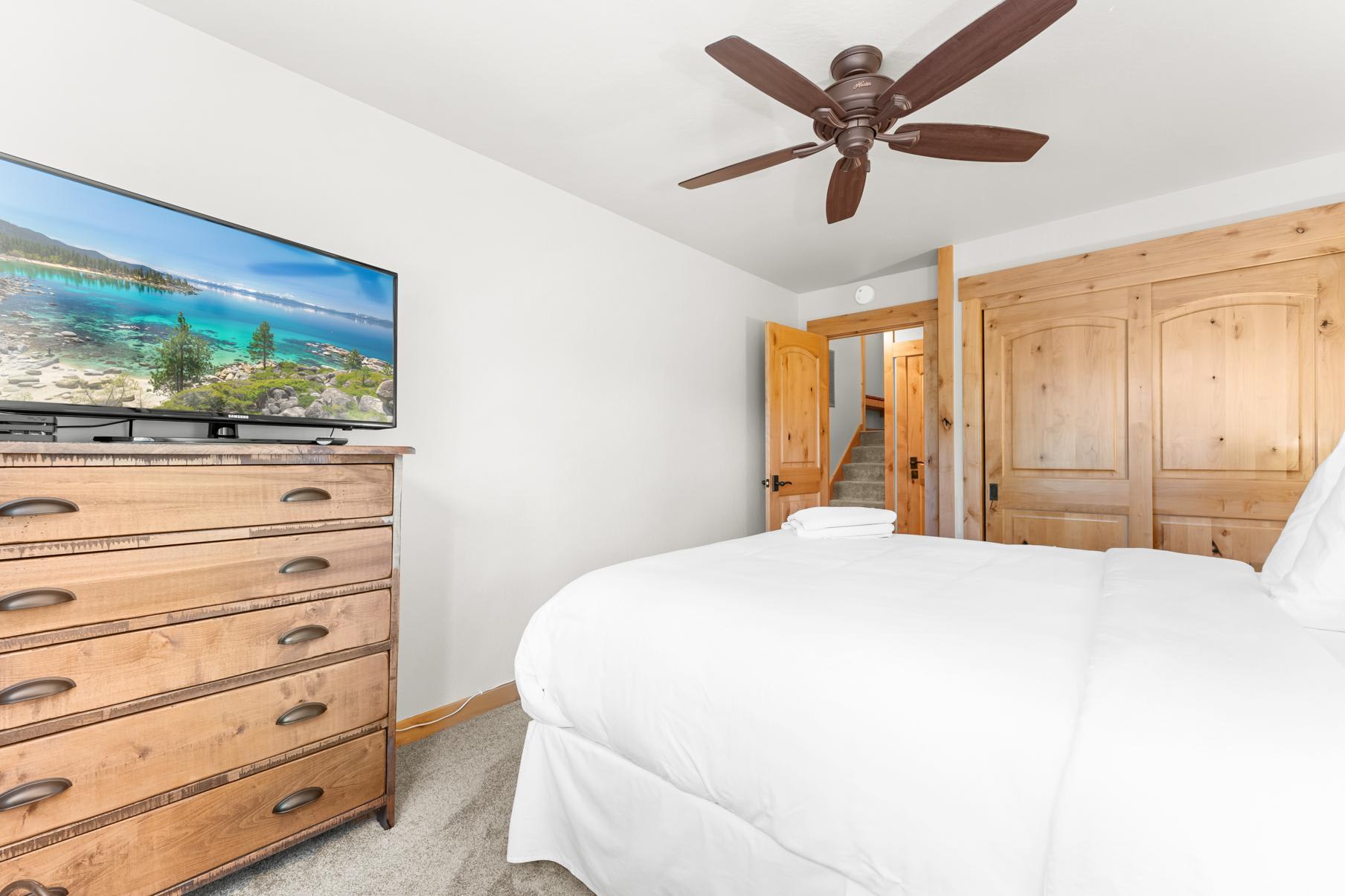 Bedroom in a Truckee vacation rental with a ceiling fan, wooden dresser, and a flat-screen TV showcasing a nature scene.