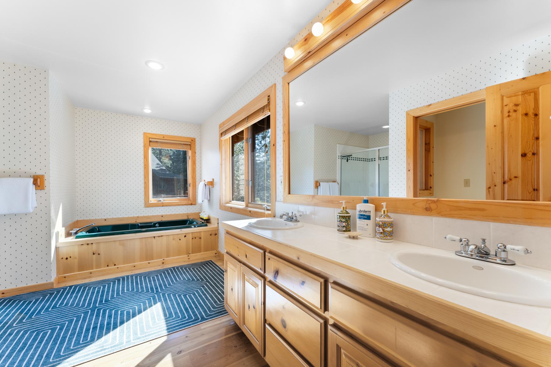 Bathroom in a Truckee vacation rental featuring a double vanity, large mirror, tub, shower, and wooden cabinetry.