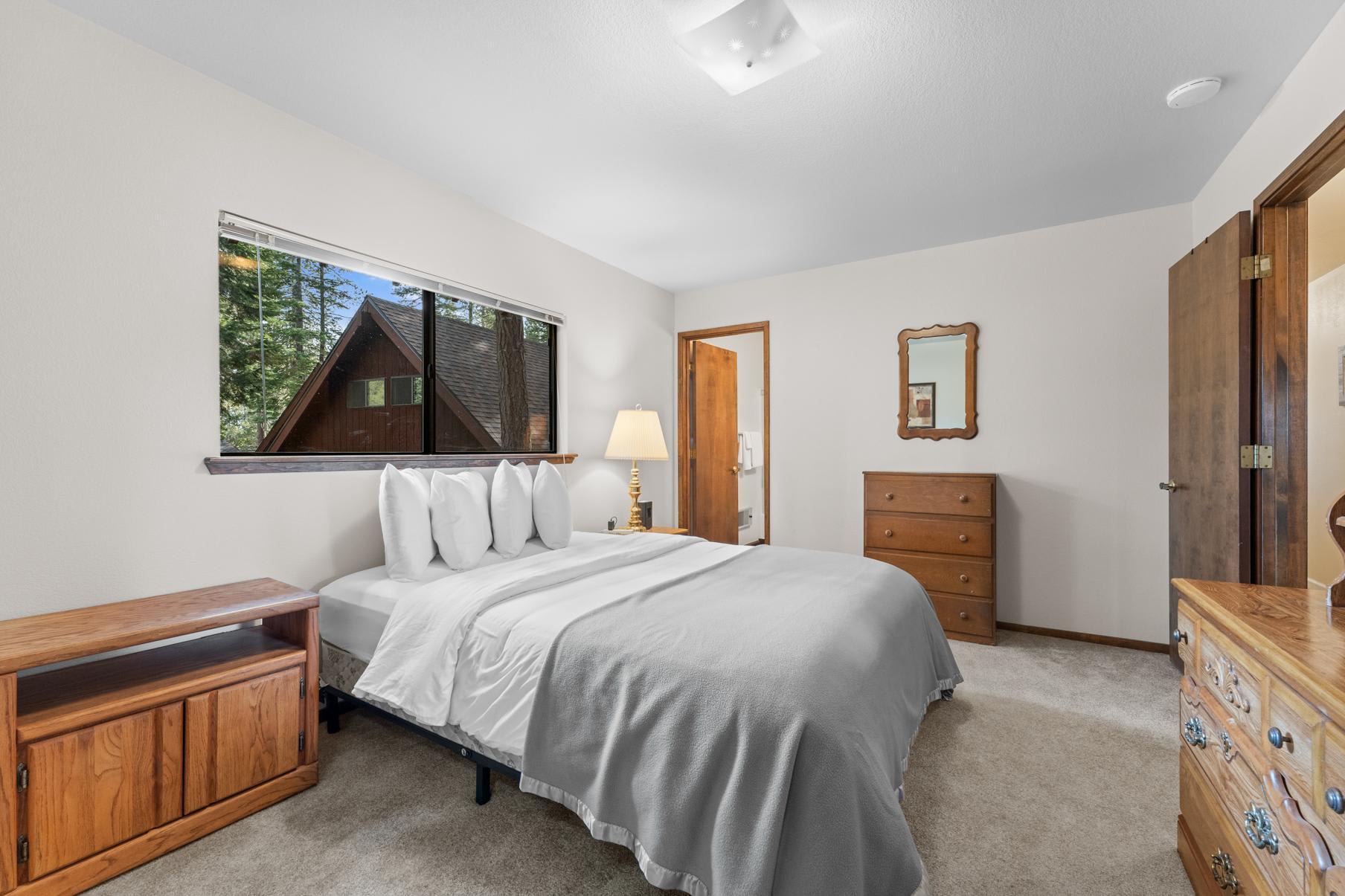 Cozy bedroom in a Truckee vacation rental, featuring a neatly made bed, wooden furniture, and a window with forest view.