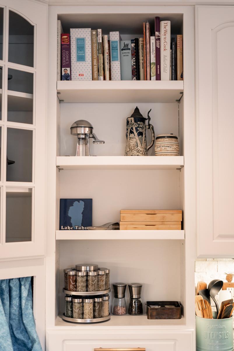 Kitchen shelf in Truckee vacation rental, displaying cookbooks, a juicer, steins, spices, and cooking utensils.