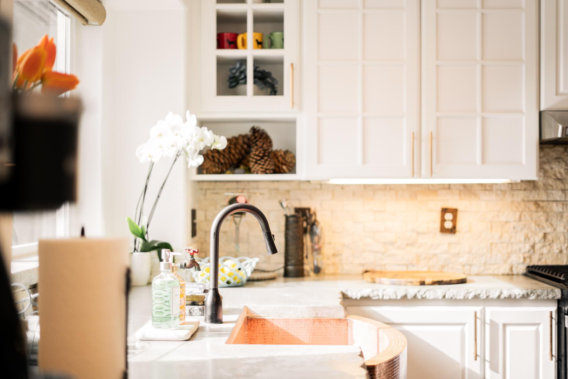 Bright kitchen in a Truckee vacation rental with white cabinets, a copper sink, orchids, and pinecone decor.