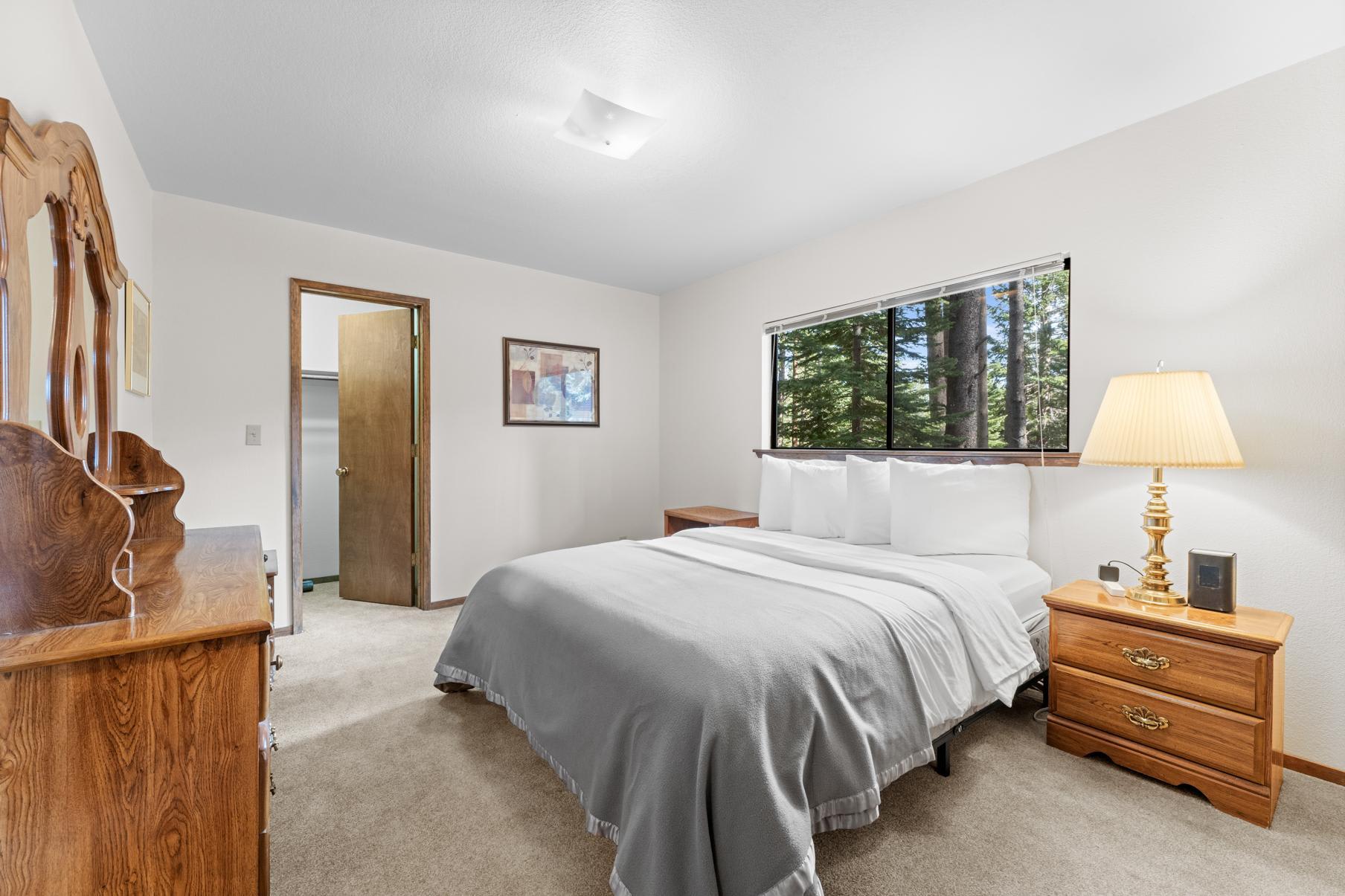 Bedroom in Truckee vacation rental with a cozy bed, wooden furniture, and a scenic forest view through the window.