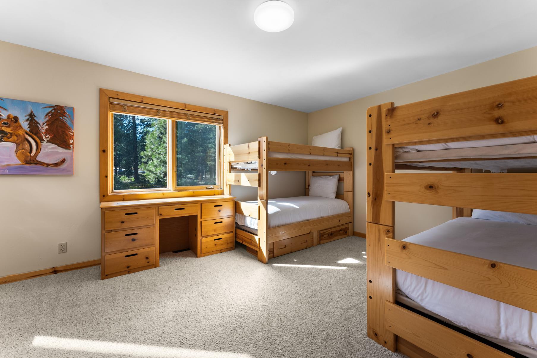 Bunk beds and wooden desk in a bright bedroom of a Truckee vacation rental, with a window view of trees.