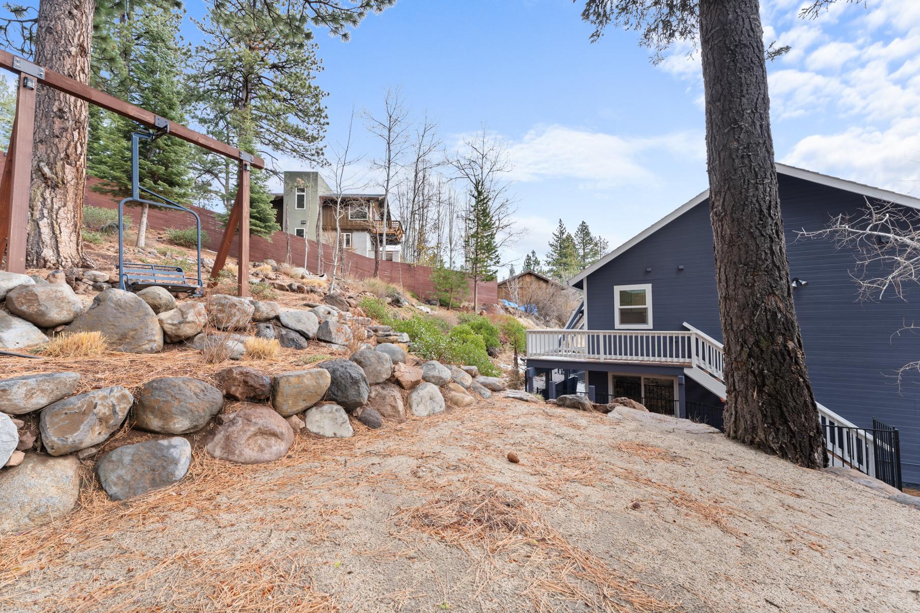 Truckee vacation rental with wooded backyard, large rocks, and a modern house under a clear blue sky.