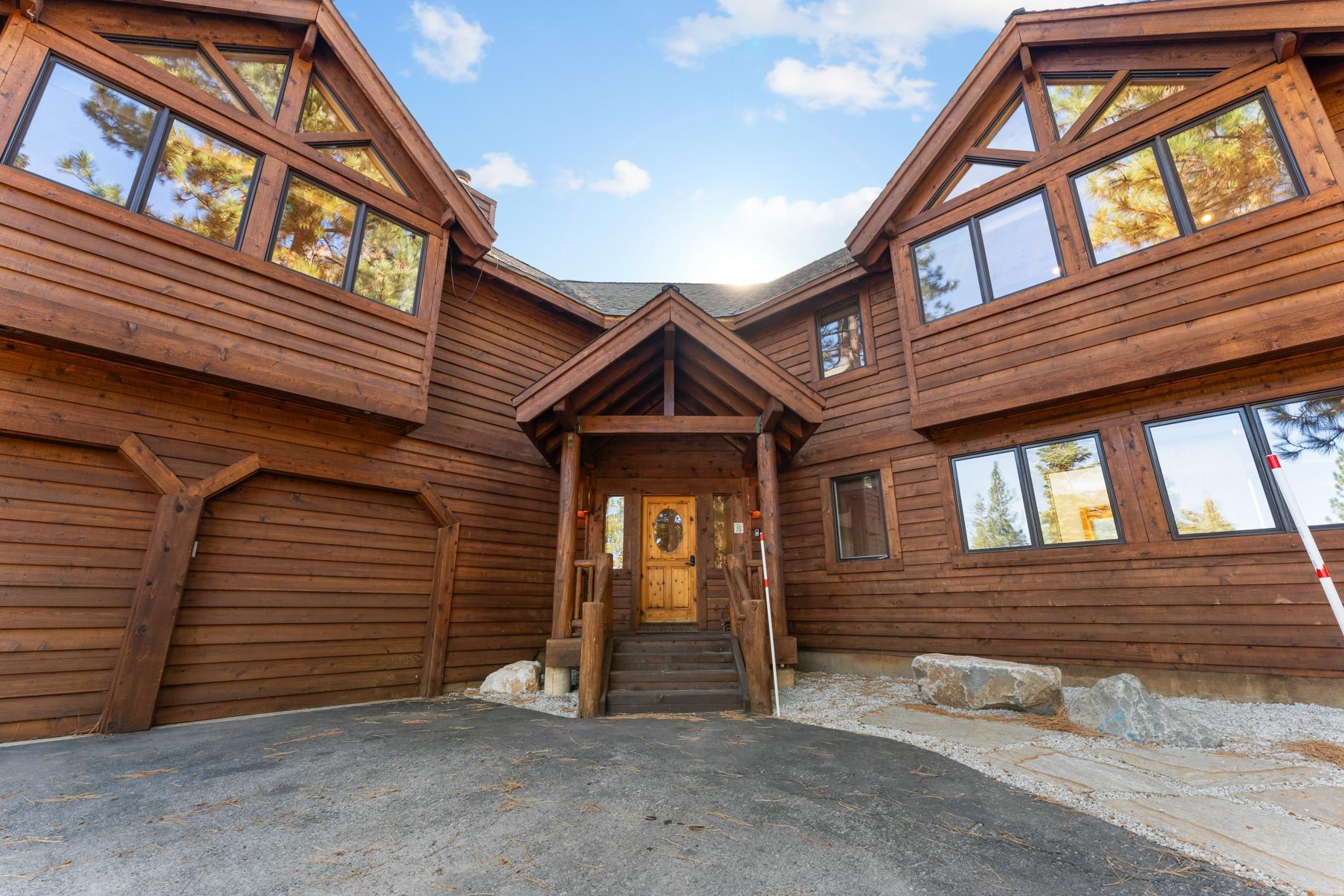 A spacious wooden cabin vacation rental in Truckee, featuring large windows and a welcoming entrance under a blue sky.