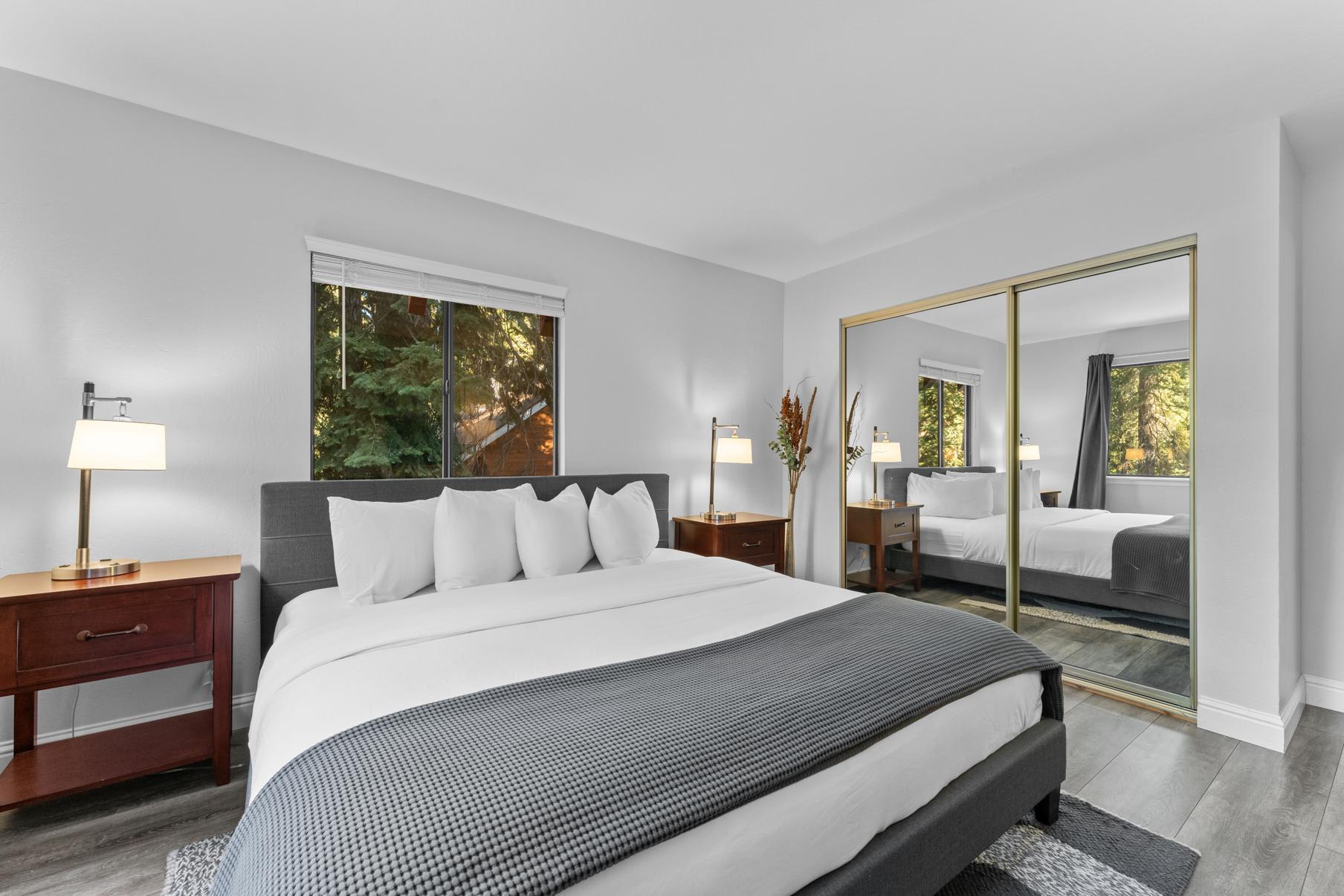 Modern bedroom in Tahoe Vista vacation rental, featuring cozy bed, mirrored closet, and forest views through window.