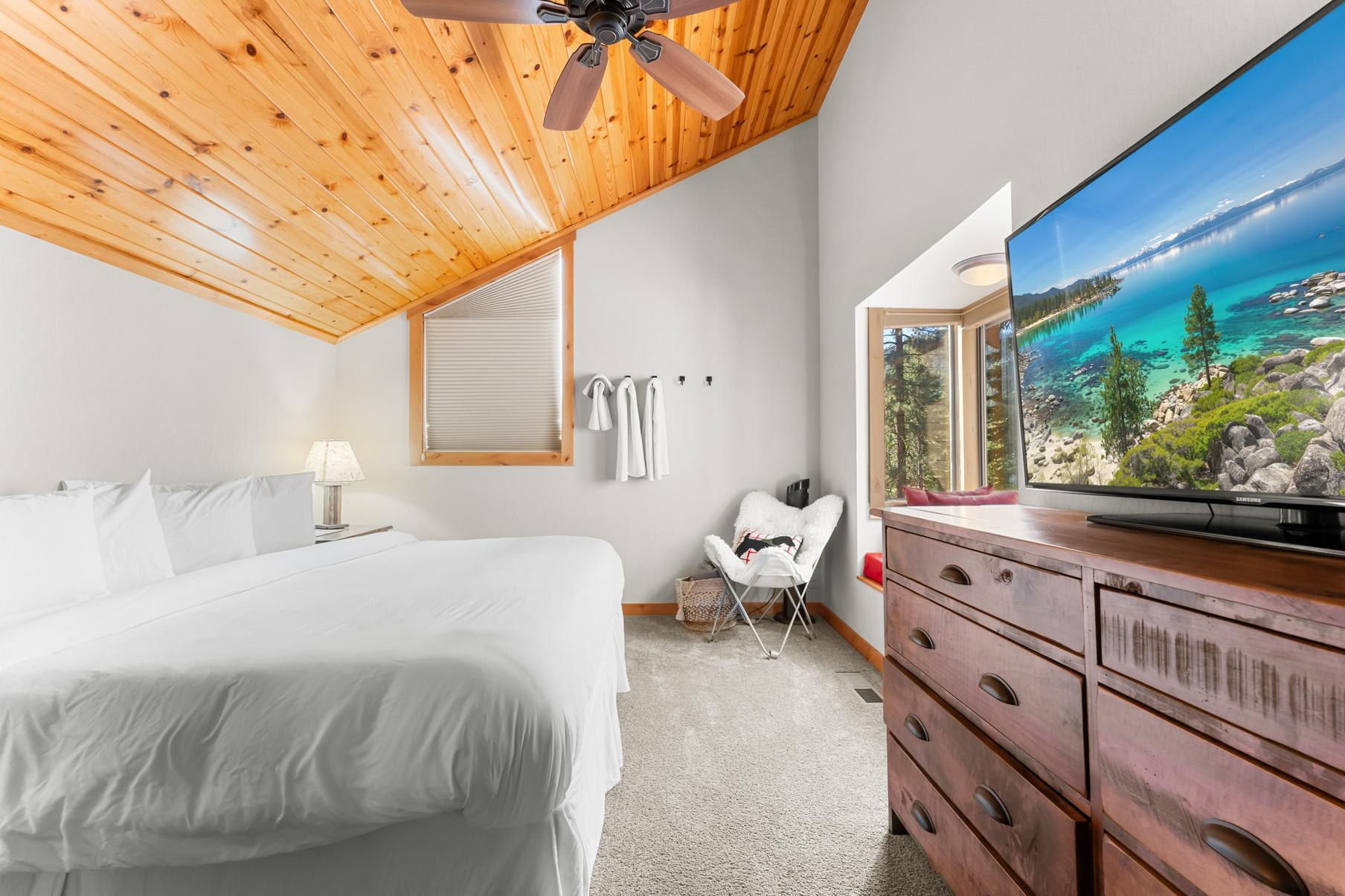 Cozy bedroom in Truckee vacation rental with wood ceiling, large bed, dresser, and scenic TV view of a lake.