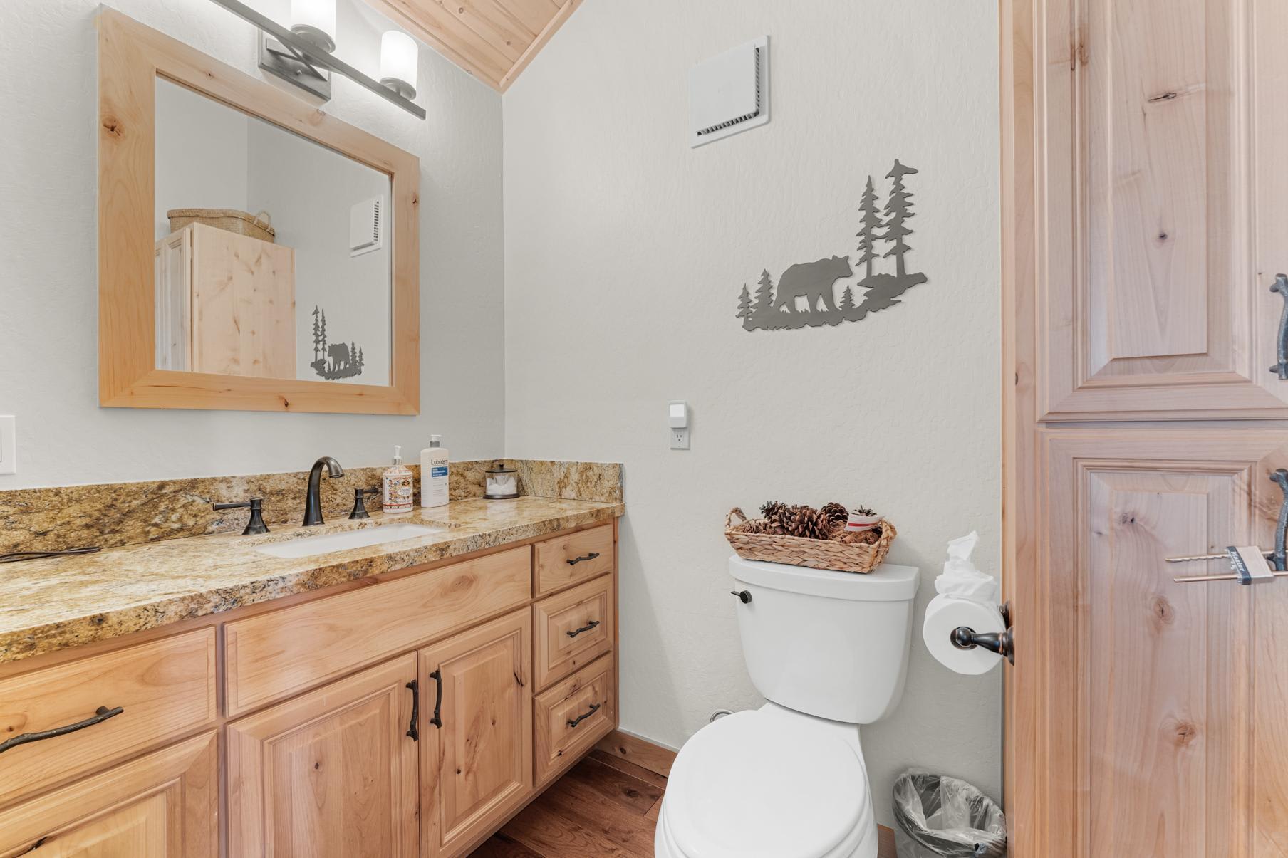 Rustic bathroom in a Truckee vacation rental with wooden cabinets, granite countertop, and bear decoration.