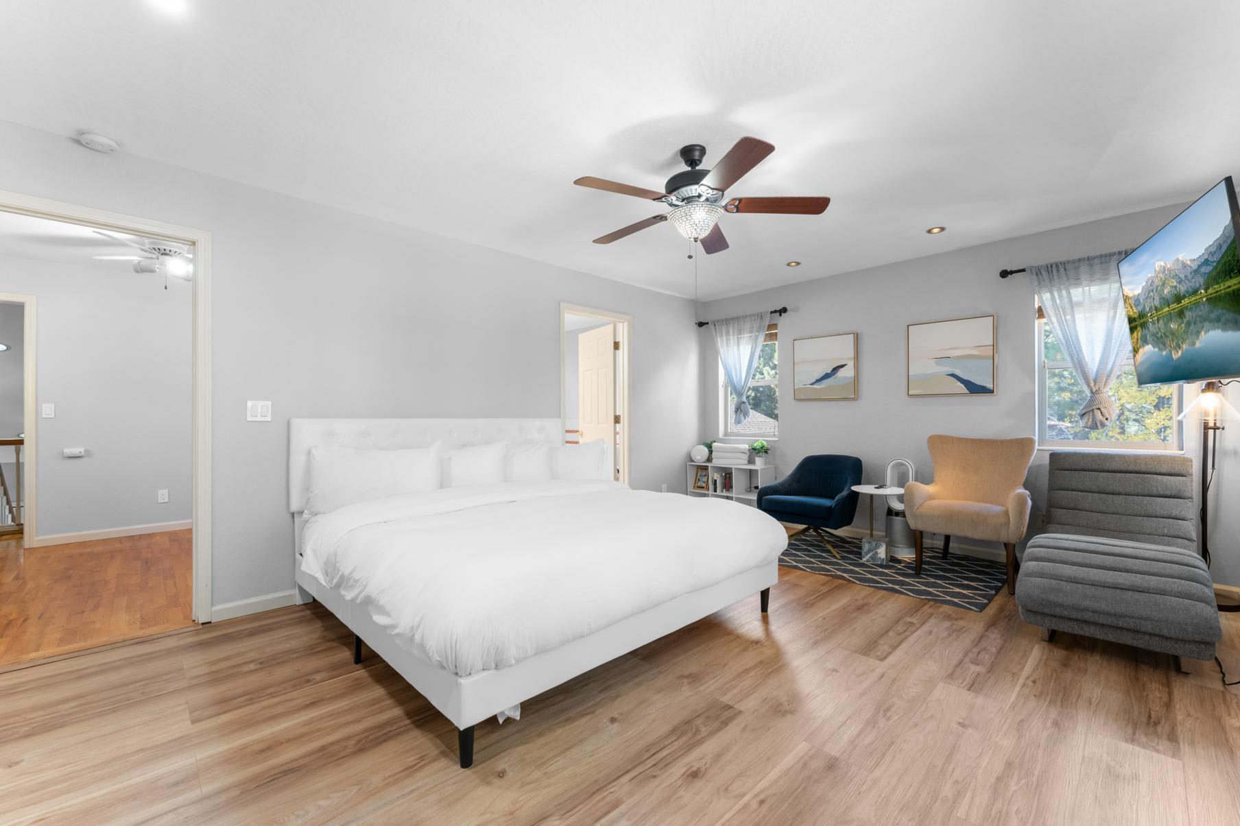 Modern bedroom in Truckee vacation rental with a cozy bed, seating area, TV, and large windows.