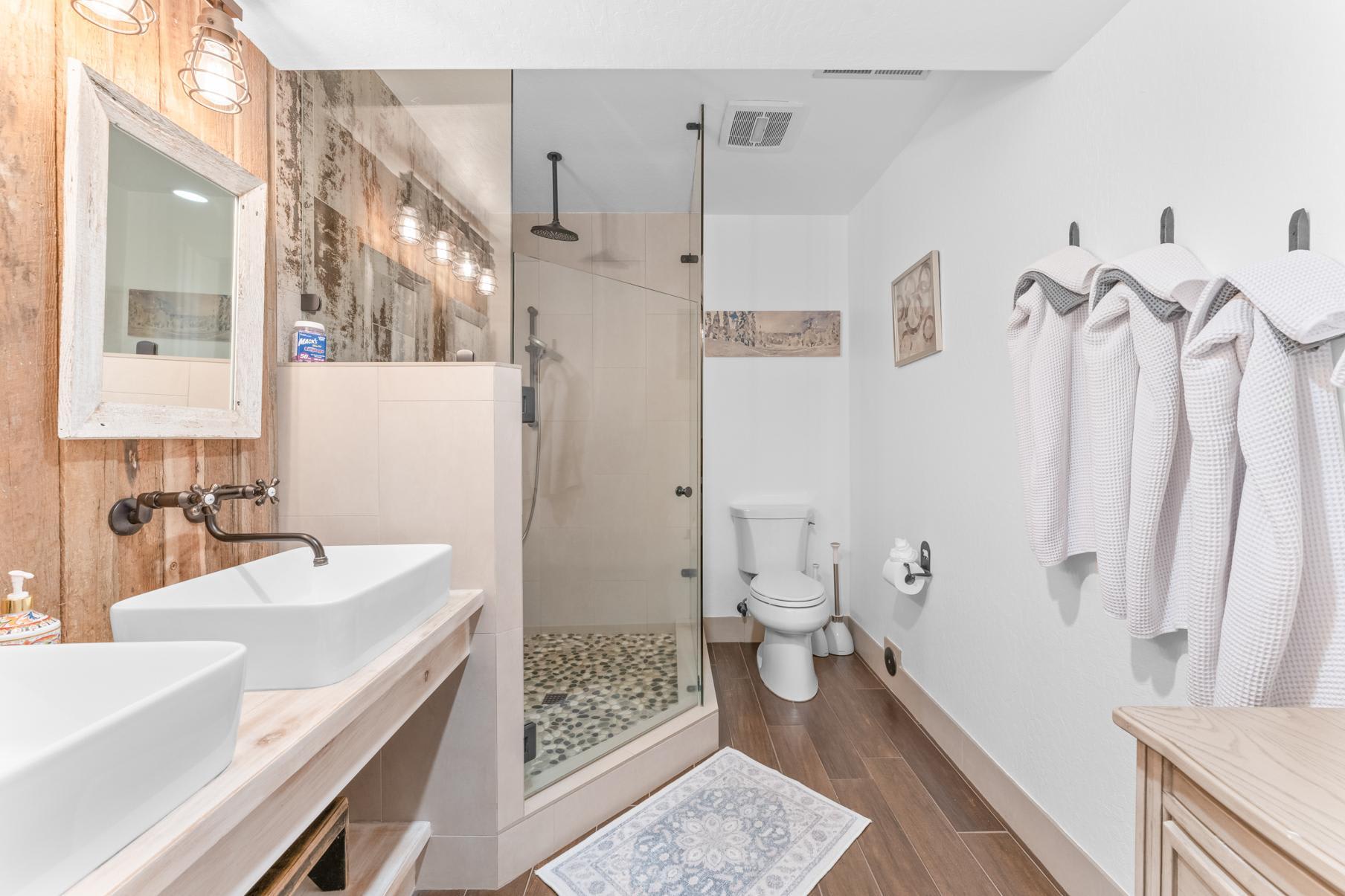 Modern bathroom in a Truckee vacation rental with double sinks, glass shower, and wooden accents.