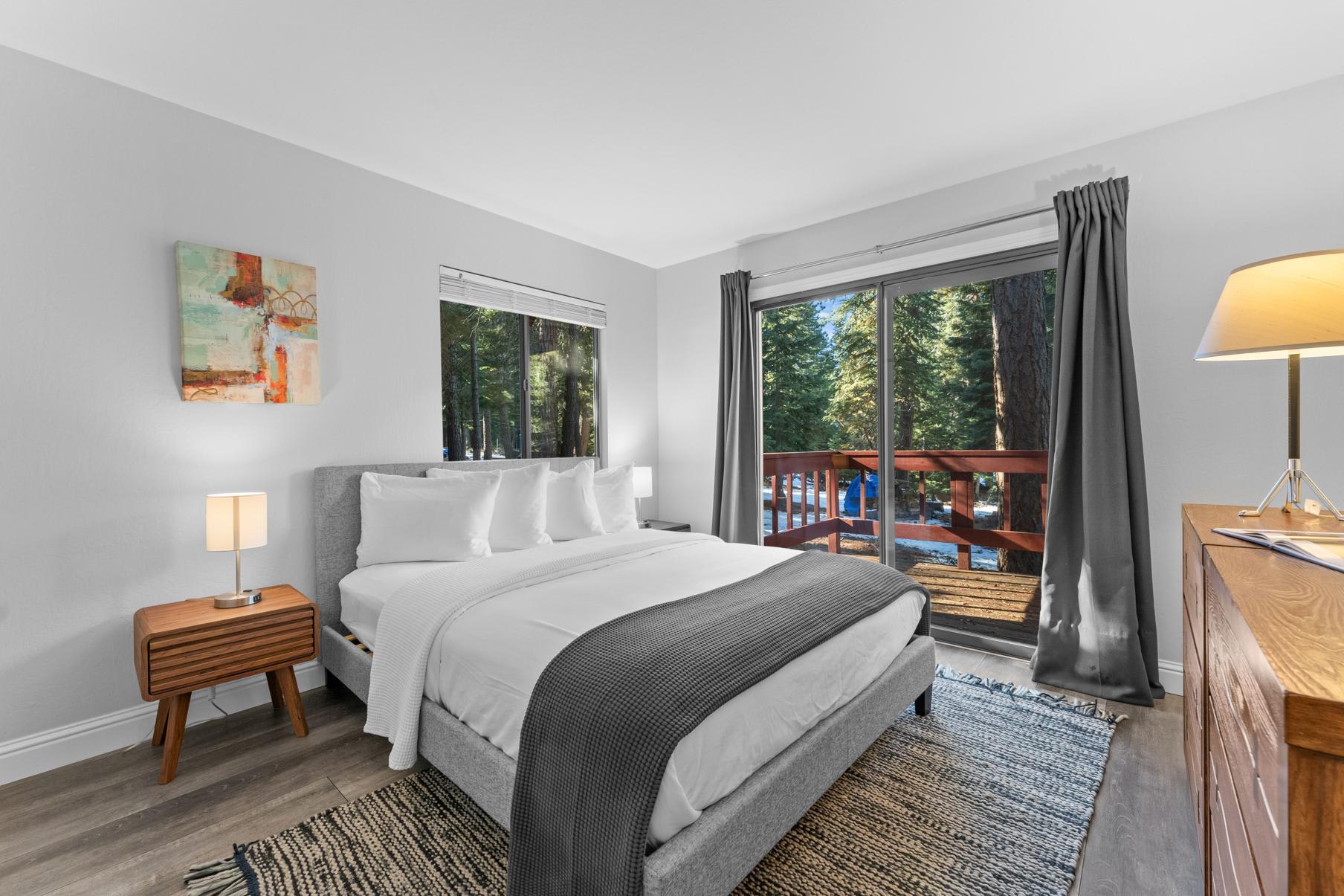 Bedroom with large windows and forest views in a Tahoe Vista vacation rental, featuring a cozy bed and modern decor.