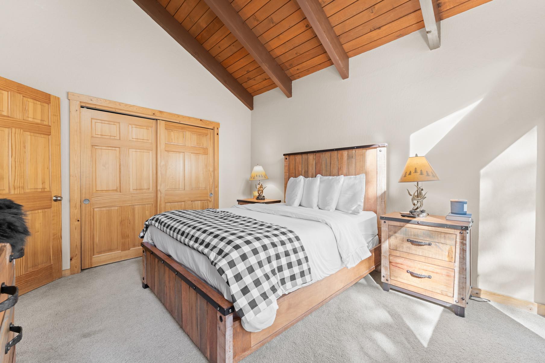 Cozy bedroom in Truckee vacation rental with wooden furniture, plaid blanket, and vaulted ceiling.