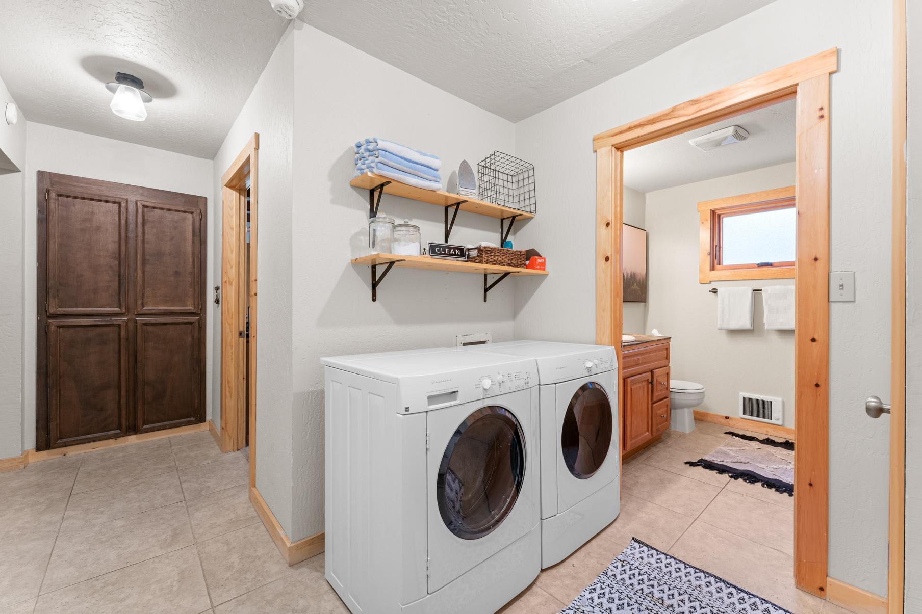 Laundry area in Truckee vacation rental with washer, dryer, shelves, and adjacent bathroom. Rustic wood accents throughout.