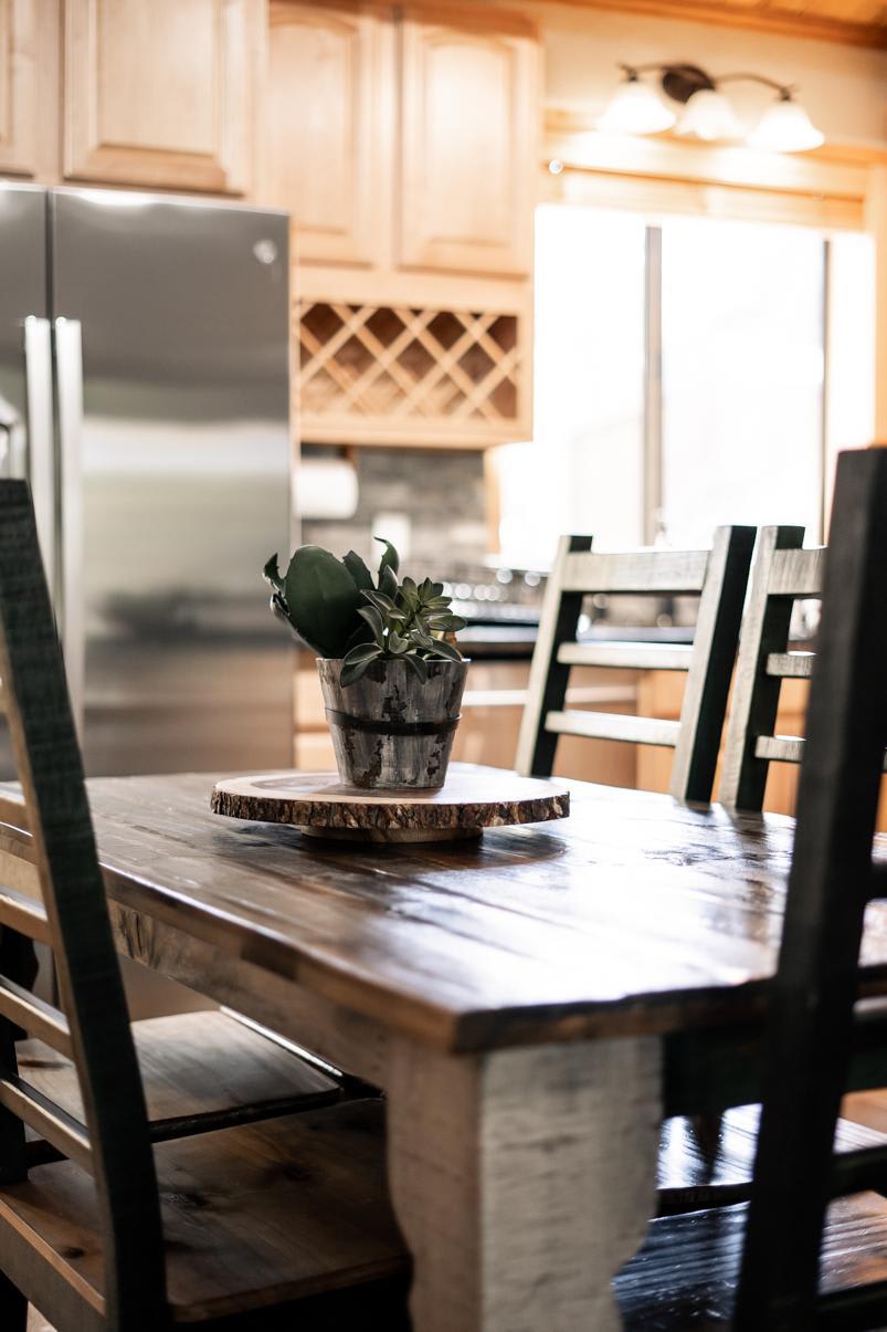 Rustic kitchen table with plants in a Truckee vacation rental, featuring wooden cabinets and a stainless steel fridge.