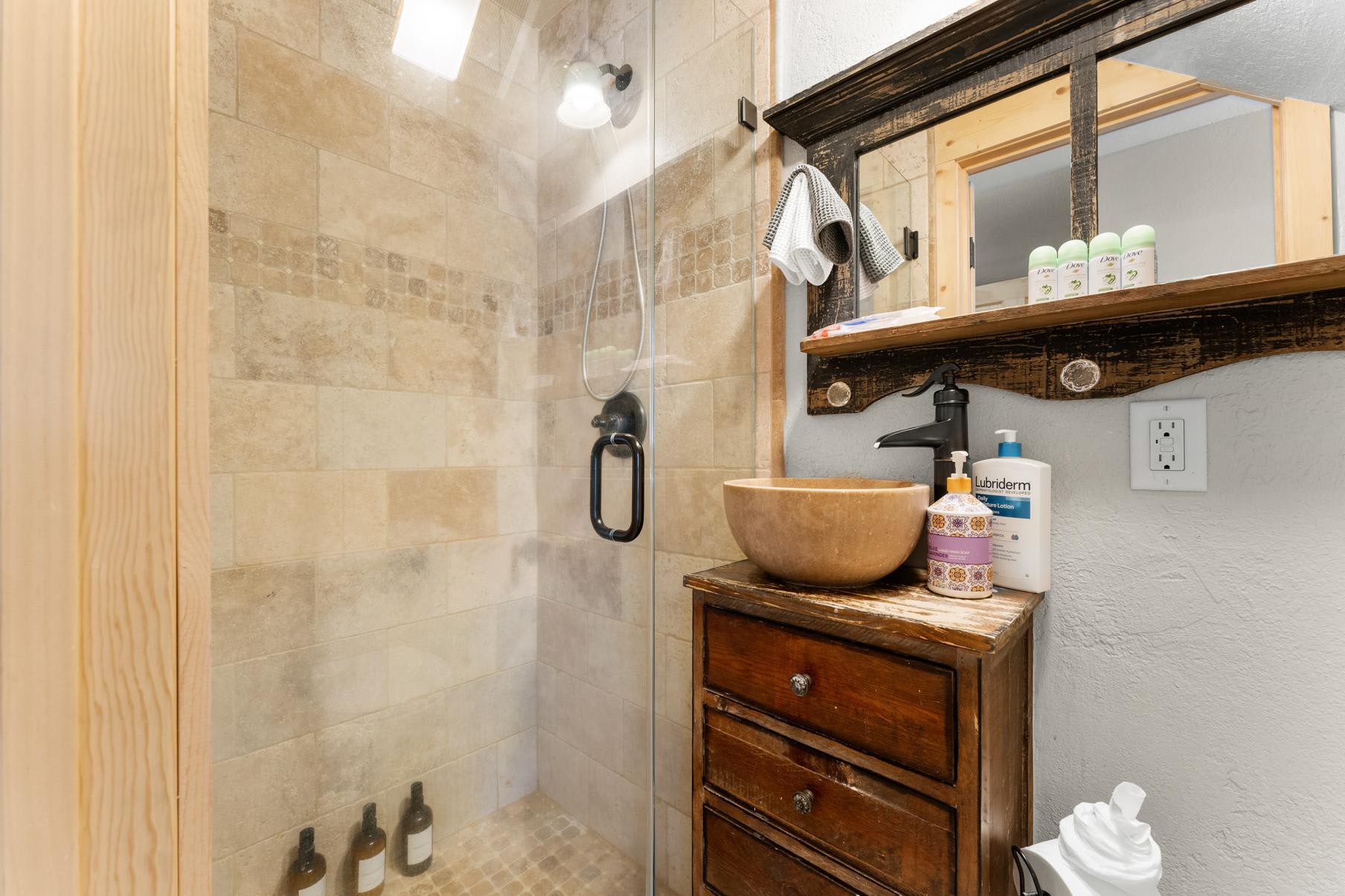 Rustic bathroom in Truckee vacation rental with wood vanity, stone vessel sink, and tiled shower.