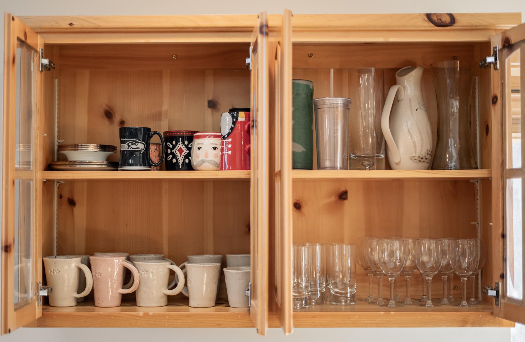 Open kitchen cabinet in a Truckee vacation rental, displaying mugs, glasses, and a pitcher.