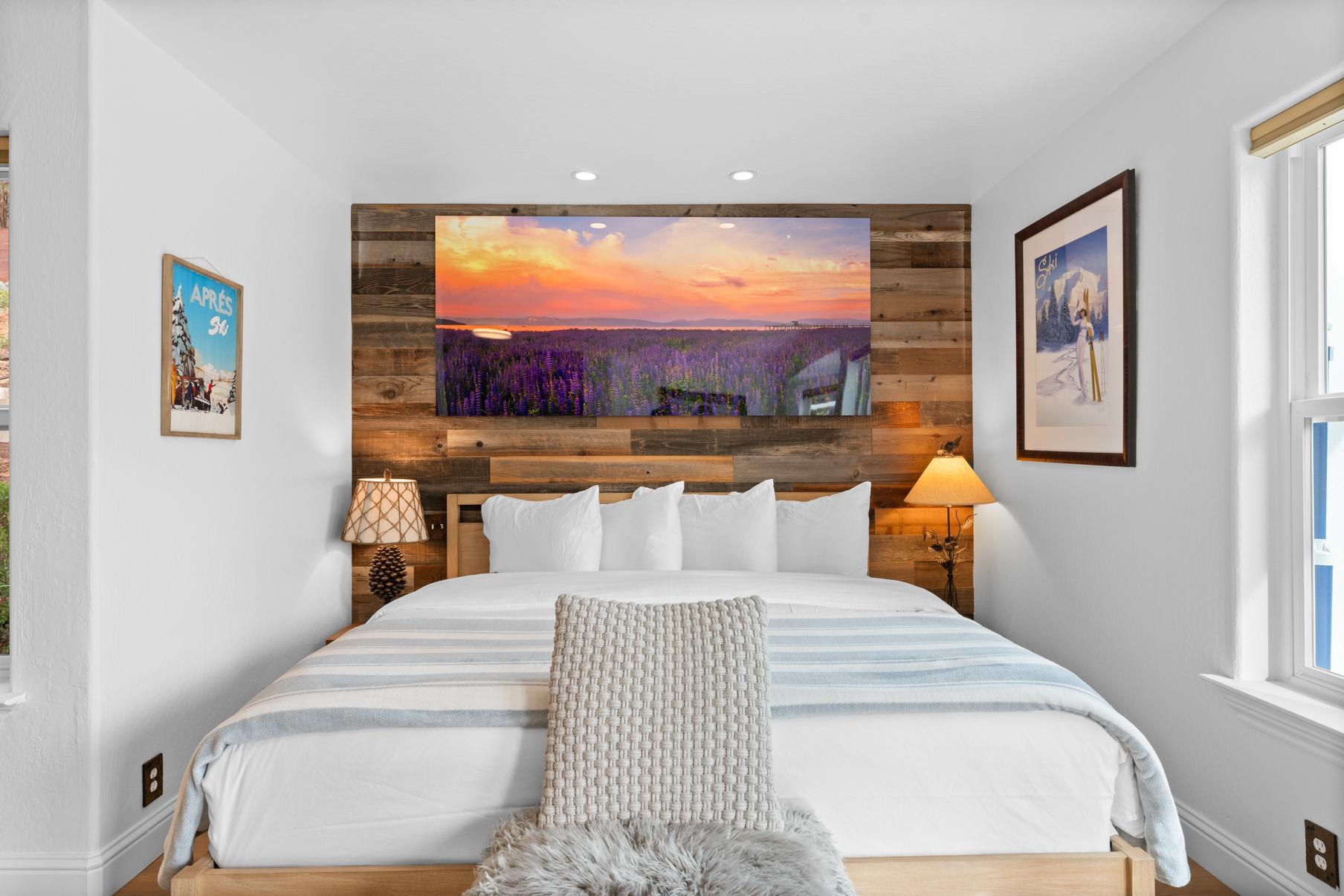 Cozy bedroom in a Truckee vacation rental, featuring a large bed, warm lighting, and scenic artwork on wooden walls.