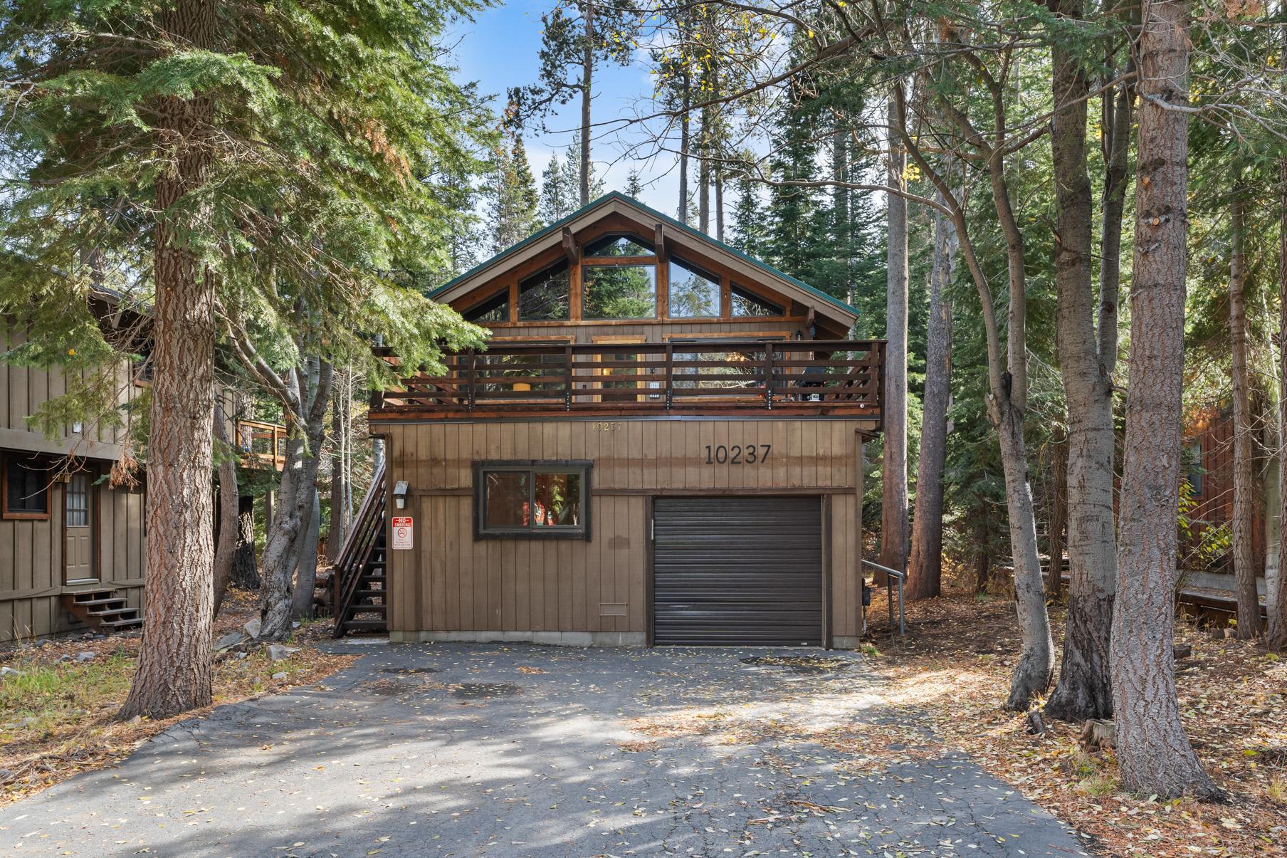 Cozy cabin-style vacation rental in Truckee, nestled among tall trees, featuring wood paneling and large windows.