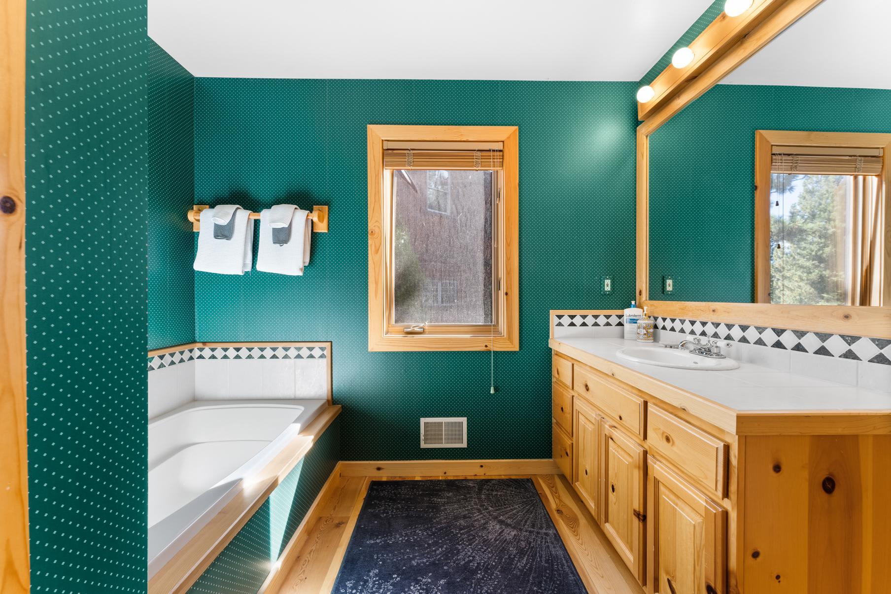 Cozy bathroom in Truckee vacation rental with green walls, wooden accents, tub, and double vanity.