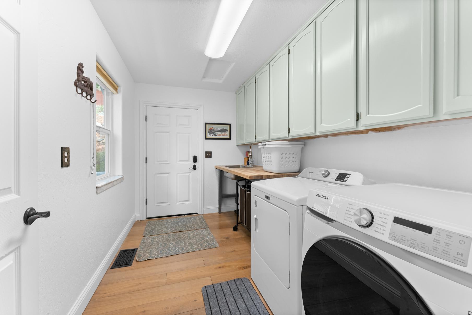 Laundry room with mint cabinets in a Truckee vacation rental, featuring washer, dryer, and wooden countertop.