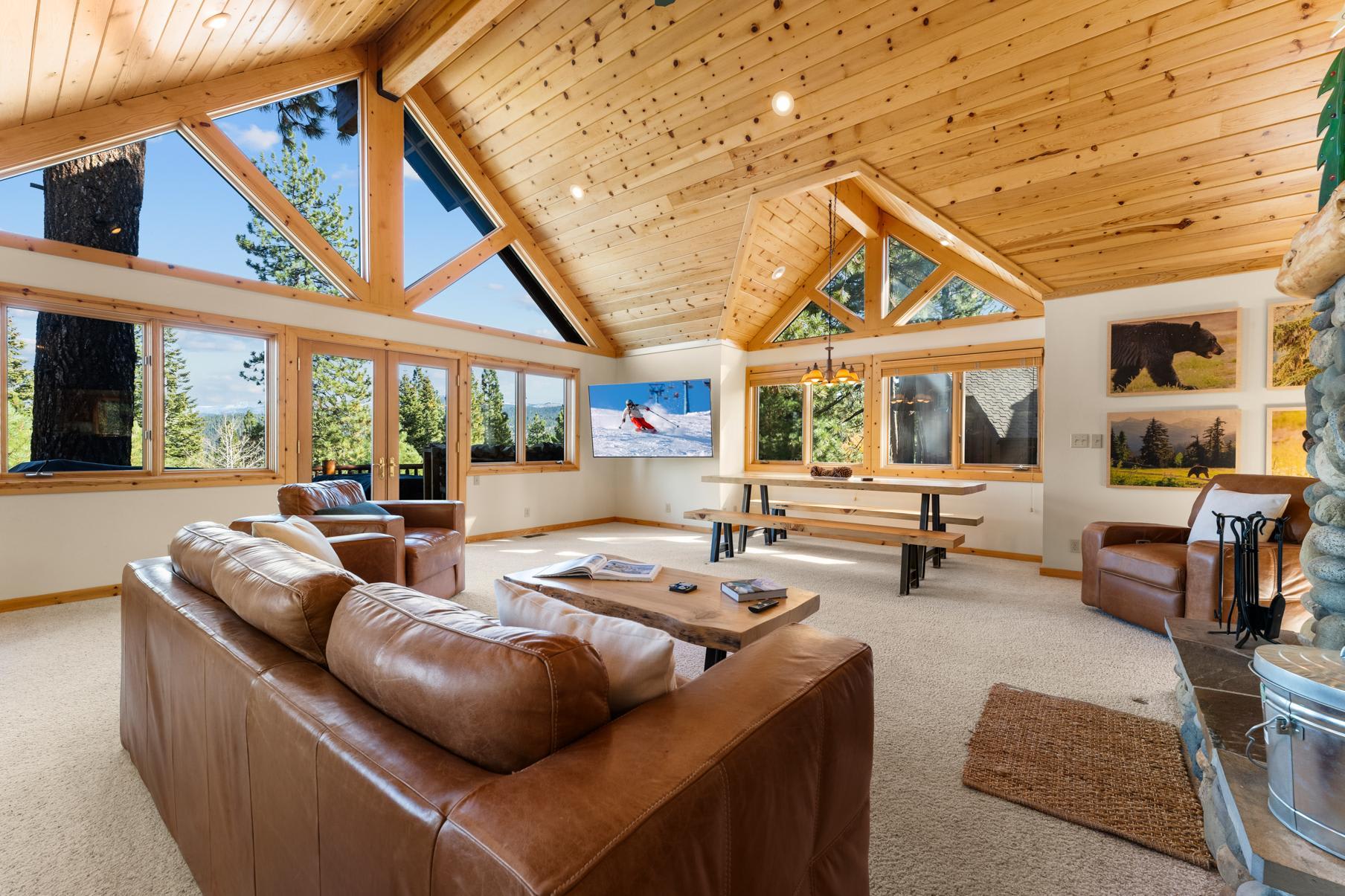 Spacious living room in a Truckee vacation rental with large windows, wooden ceiling, and leather sofas.