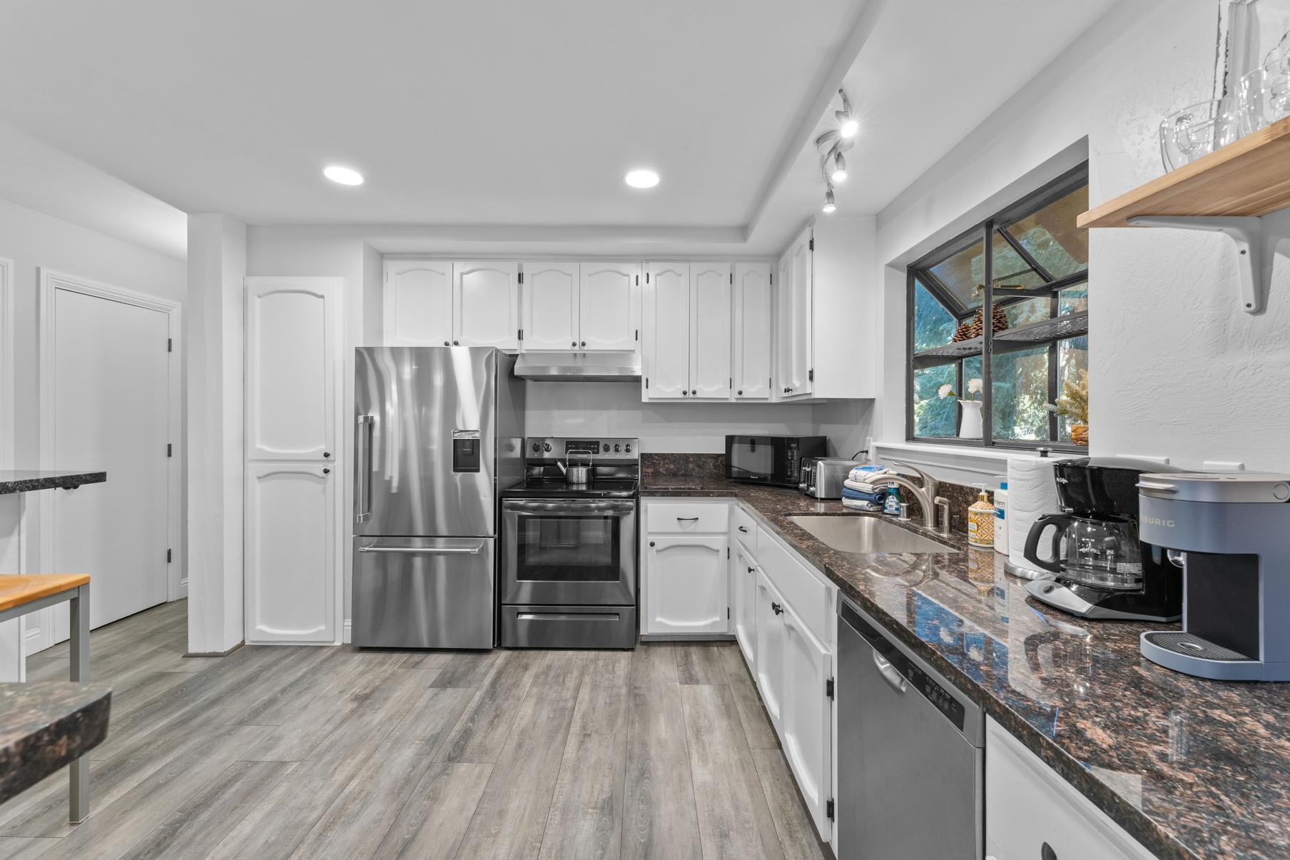 Modern kitchen in a Tahoe Vista vacation rental, featuring stainless steel appliances, white cabinets, and wood flooring.