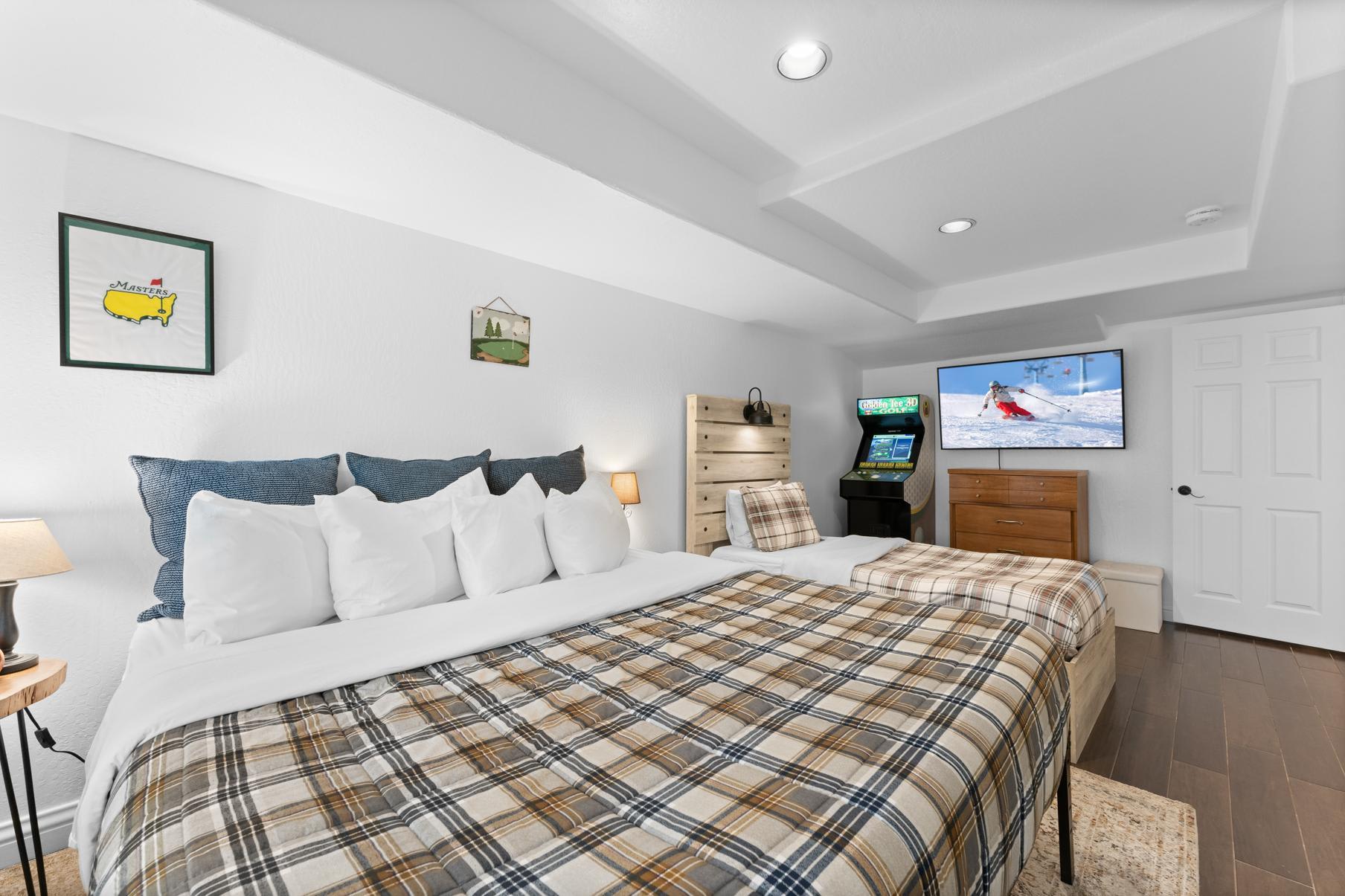 Cozy bedroom in a Truckee vacation rental with plaid bedding, snowy ski scene on TV, and an arcade game.