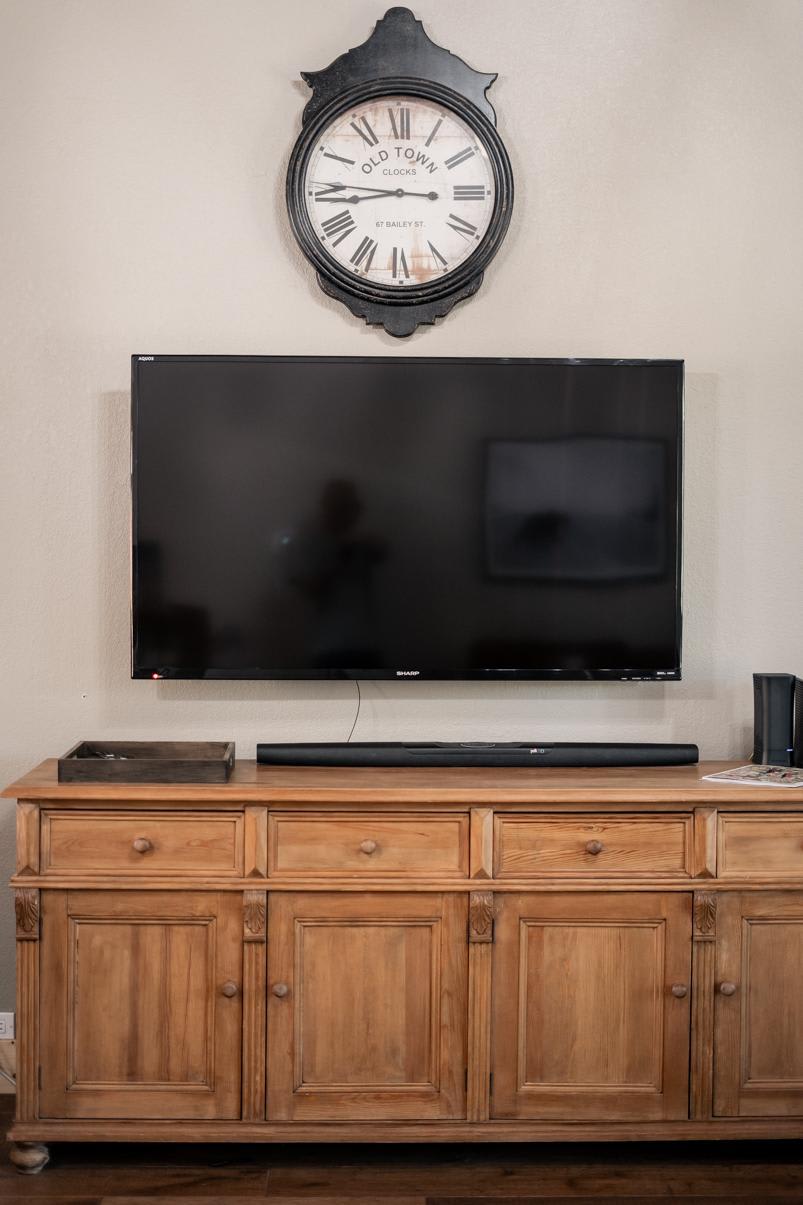 TV on rustic wooden cabinet beneath clock in Truckee vacation rental living room.