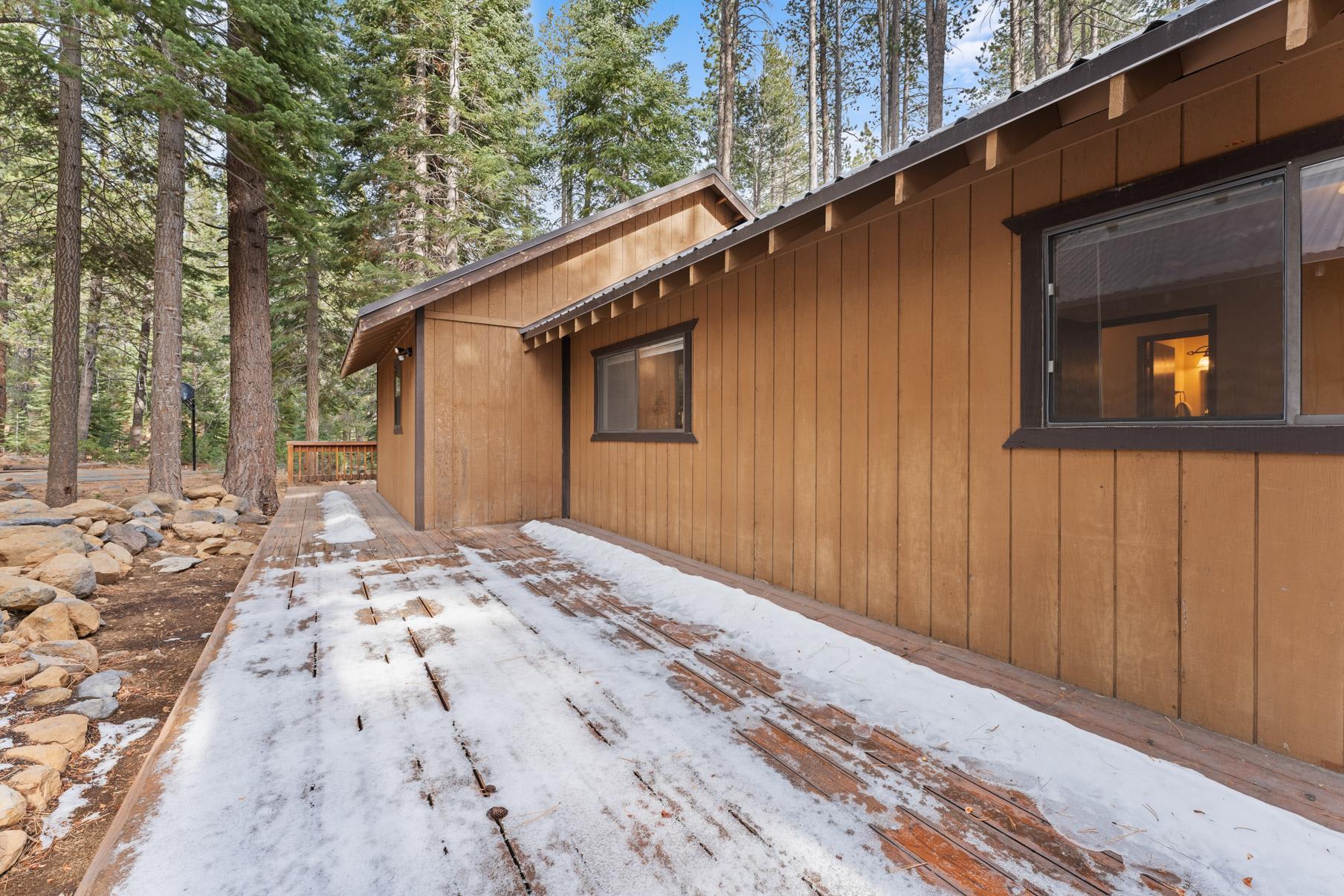 Wooden vacation rental cabin in Truckee, surrounded by tall trees, with a snowy walkway and rustic charm.