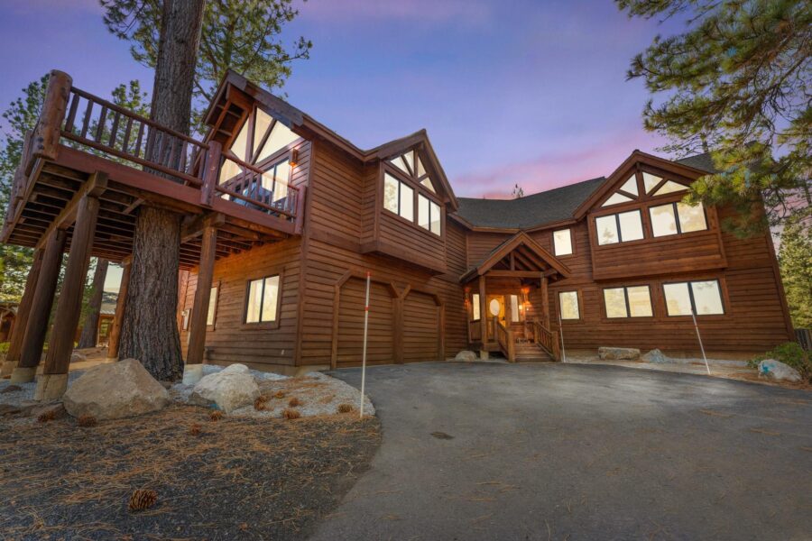 A large wooden cabin with a deck in Truckee, ideal for a vacation rental, against a colorful sunset sky.