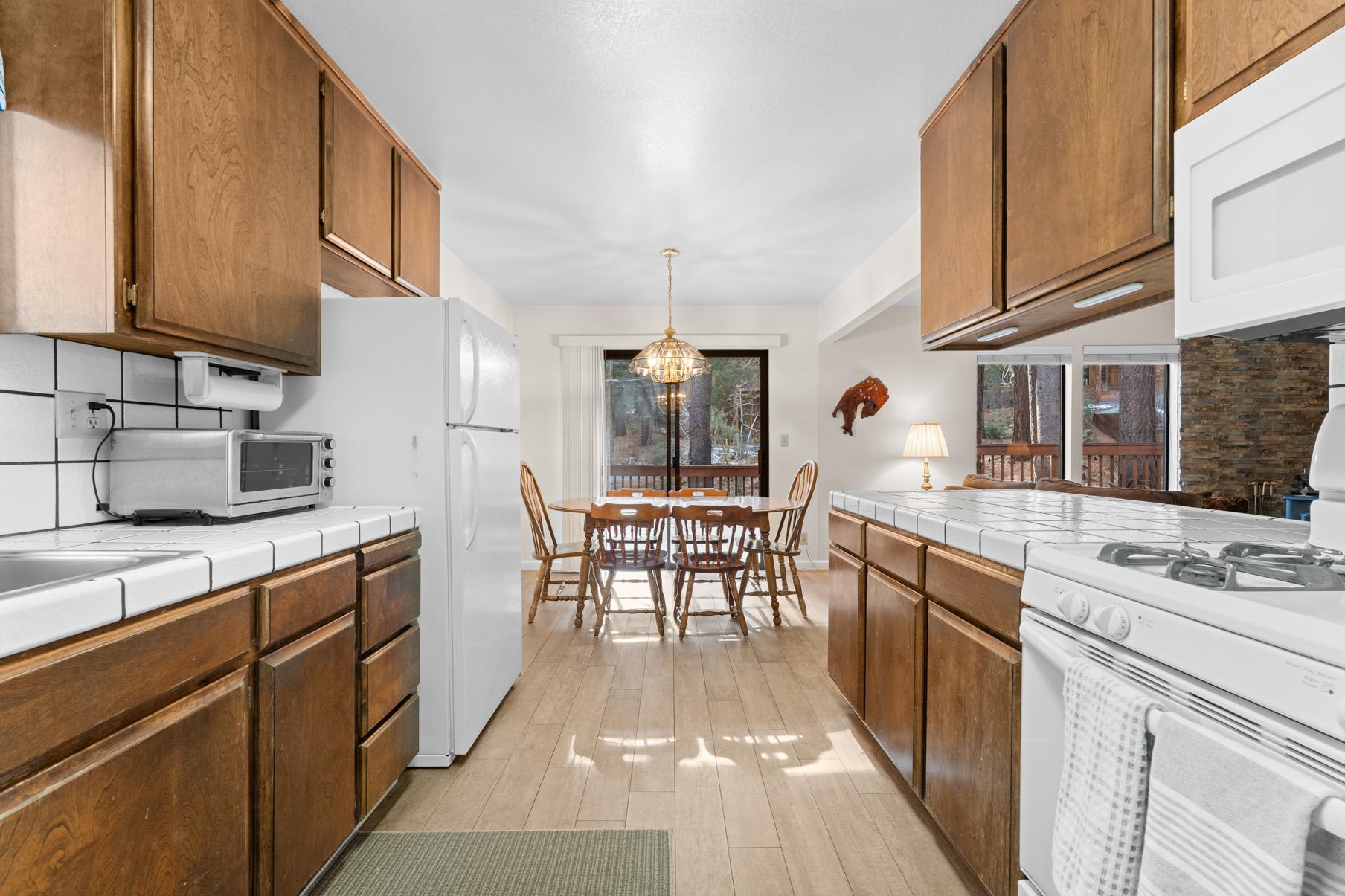 Truckee vacation rental kitchen with wooden cabinets, white appliances, and a dining area overlooking a forest view.