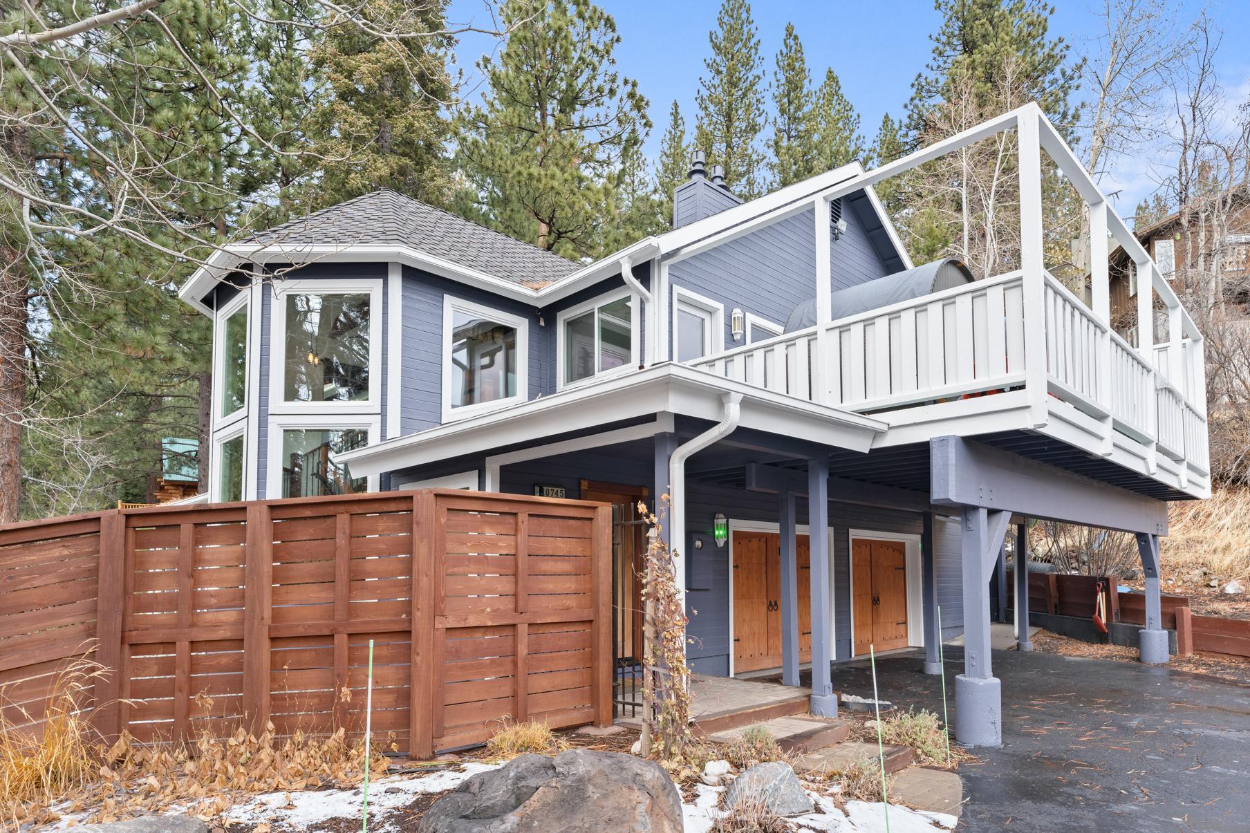 Charming blue vacation rental in Truckee with a large deck, surrounded by trees and featuring a wooden fence.