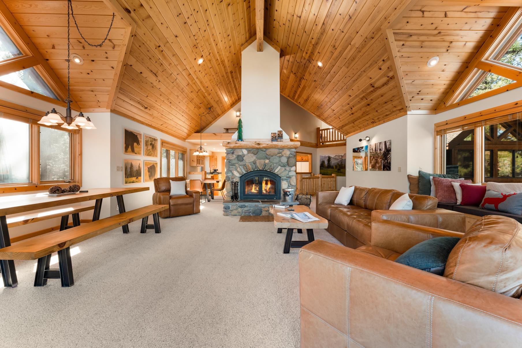 Cozy living room with stone fireplace in a Truckee vacation rental, featuring wood accents and large windows.