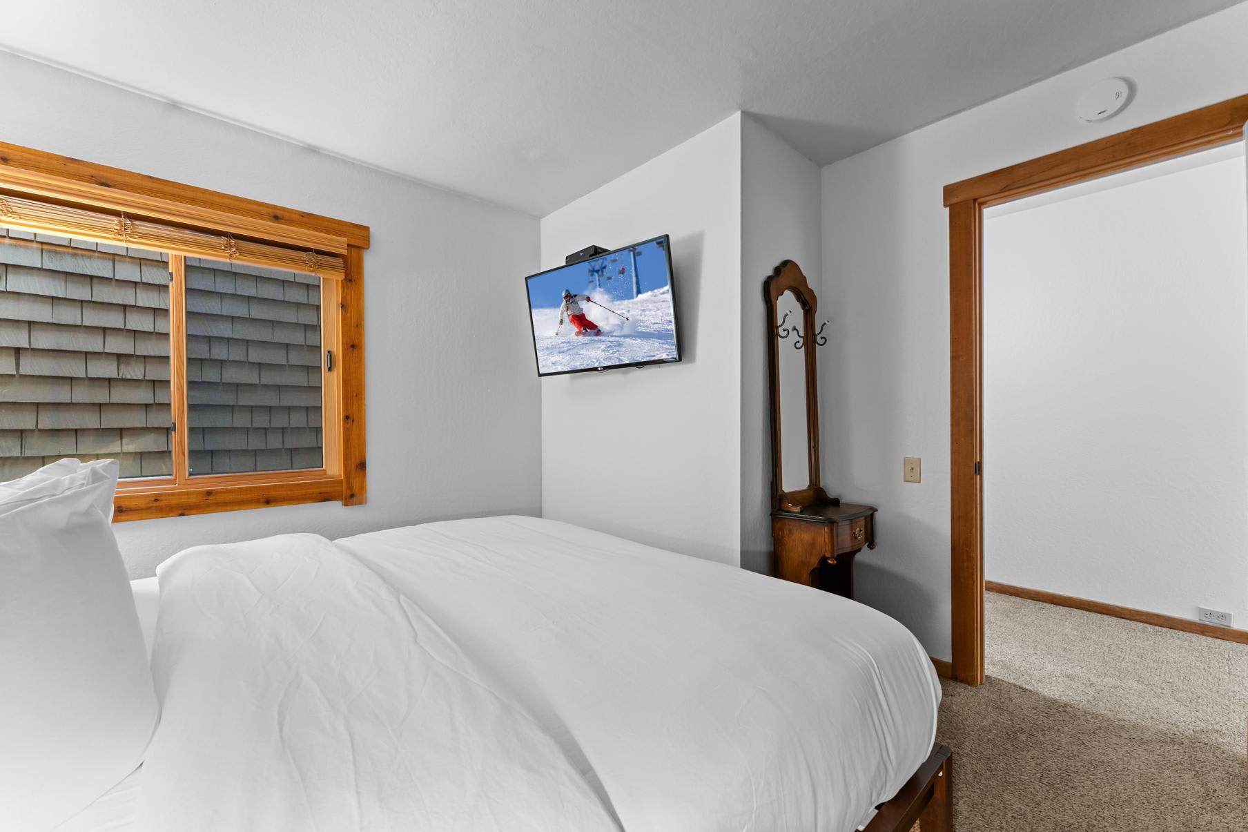 Cozy bedroom in a Truckee vacation rental, featuring a large bed, window, TV, and a small wooden vanity.