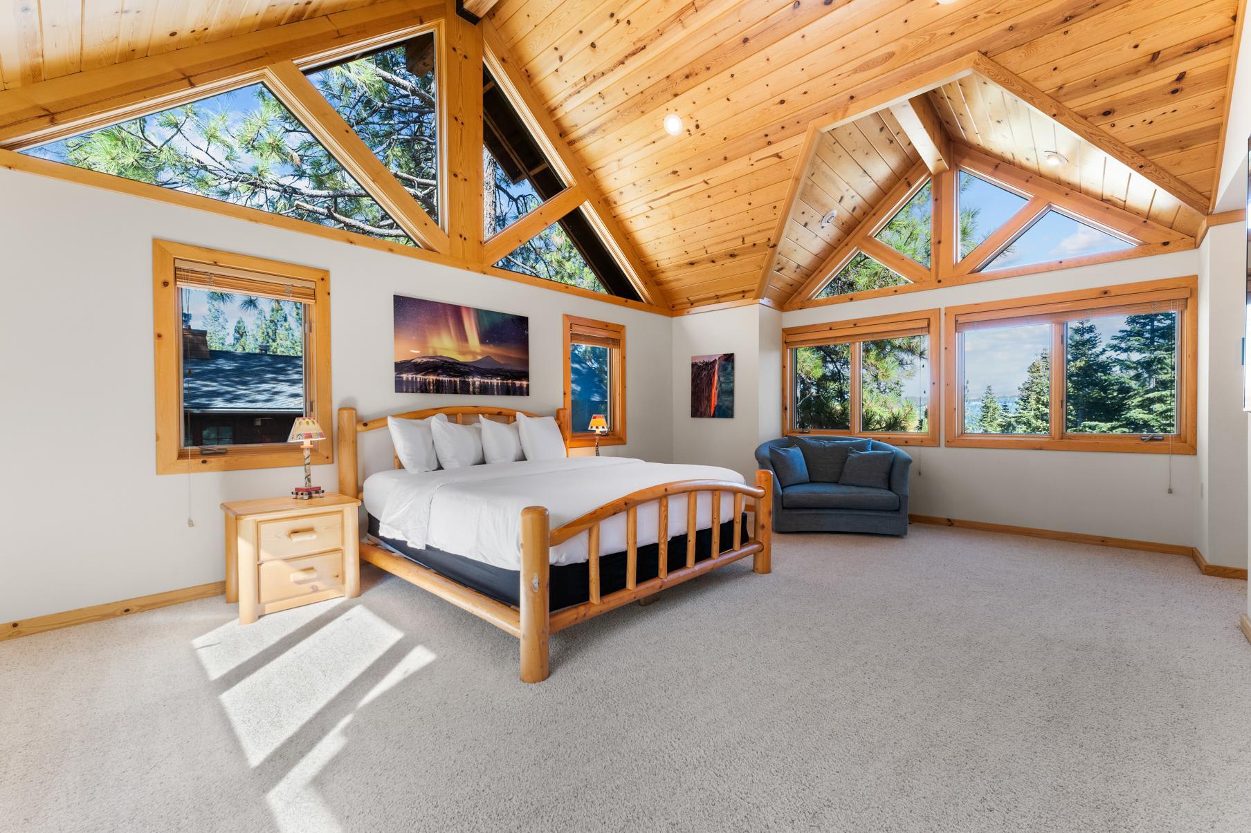 Spacious bedroom in a Truckee vacation rental with large windows, wooden ceiling, and forest views.