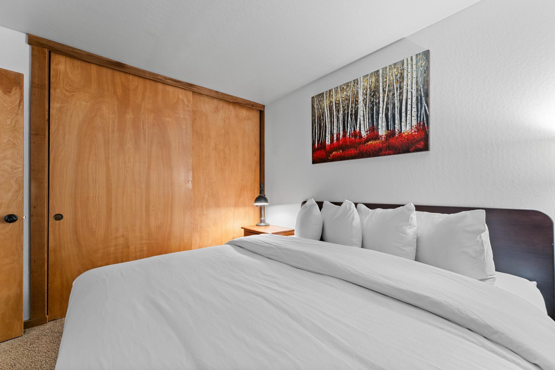 Bedroom in a Truckee vacation rental with a cozy bed, wooden closet, and a forest landscape painting on the wall.