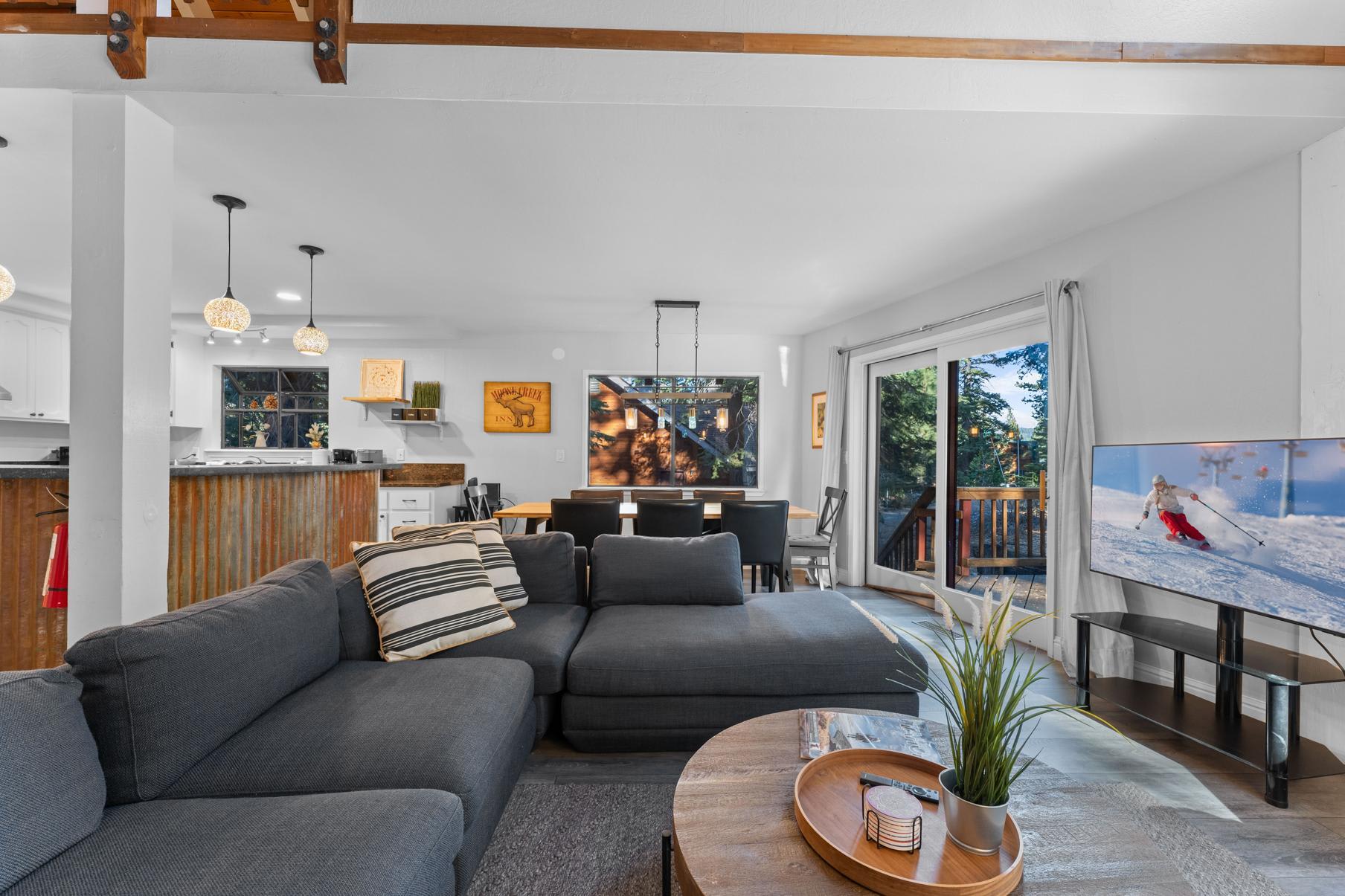 Modern living room in a Tahoe Vista vacation rental, featuring a cozy sofa, elegant dining area, and large windows with forest views.