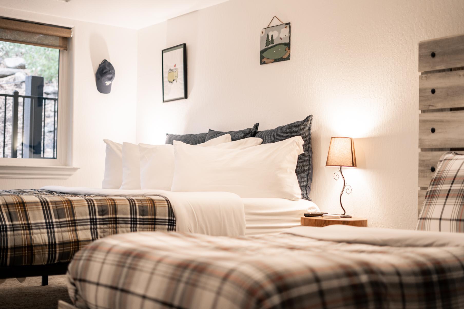 Cozy bedroom in a Truckee vacation rental with plaid bedding, a lamp, and wall art, offering a welcoming atmosphere.