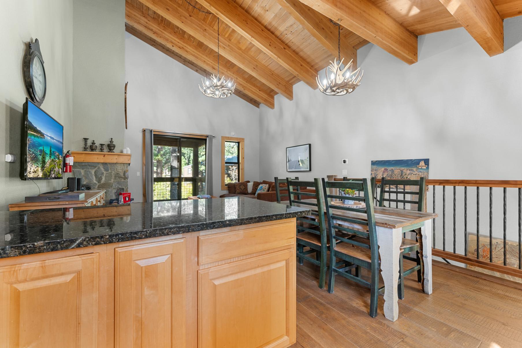 Rustic dining area in Truckee vacation rental with wooden beams, antler chandeliers, and stone fireplace.