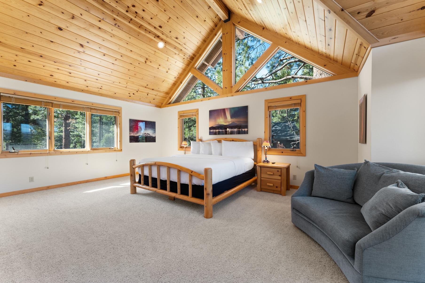 Spacious bedroom in Truckee vacation rental, featuring wooden ceilings, large windows, a cozy bed, and a plush sofa.