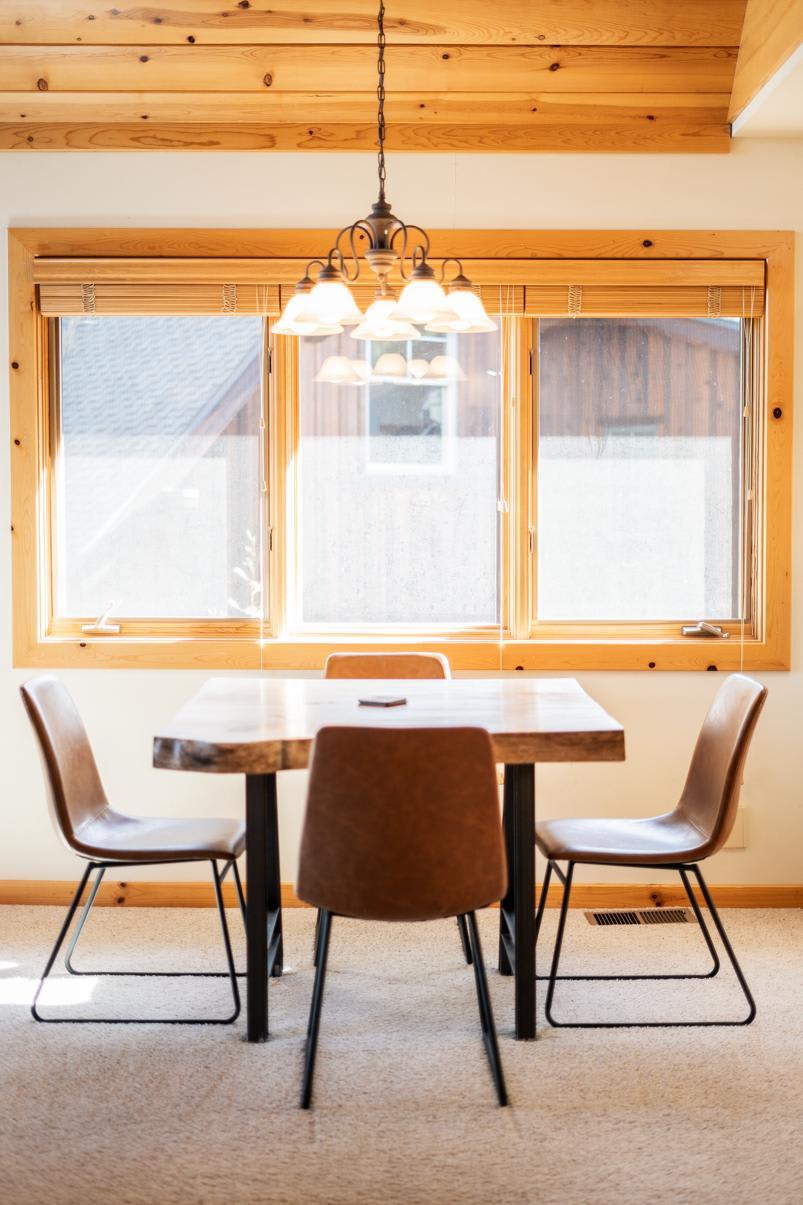 Cozy dining area in a Truckee vacation rental with a rustic table, chairs, and large wooden-framed windows.