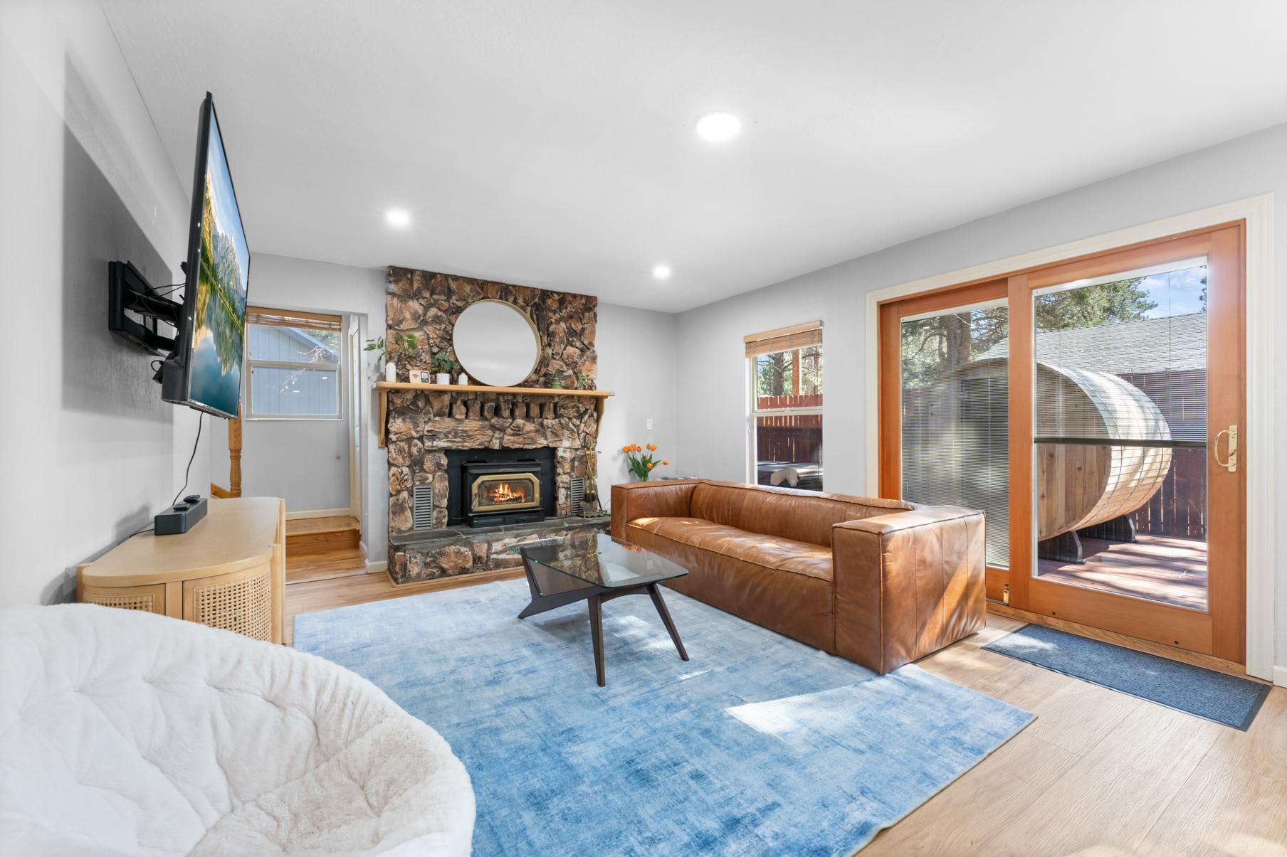 Modern Truckee vacation rental living room with stone fireplace, leather sofa, large windows, and outdoor view.