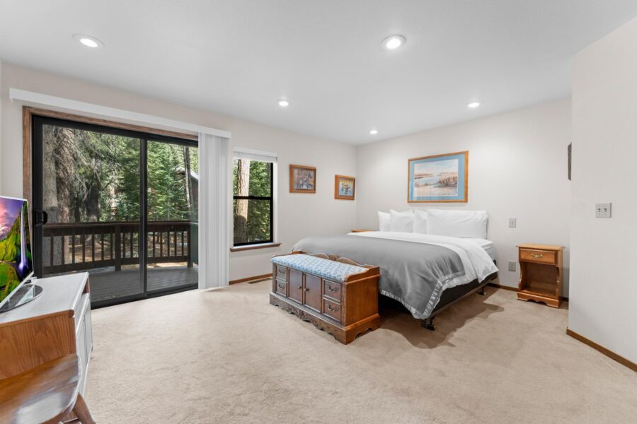 Spacious bedroom in Truckee vacation rental with a king bed, art on walls, and a sliding door leading to a forest-view deck.