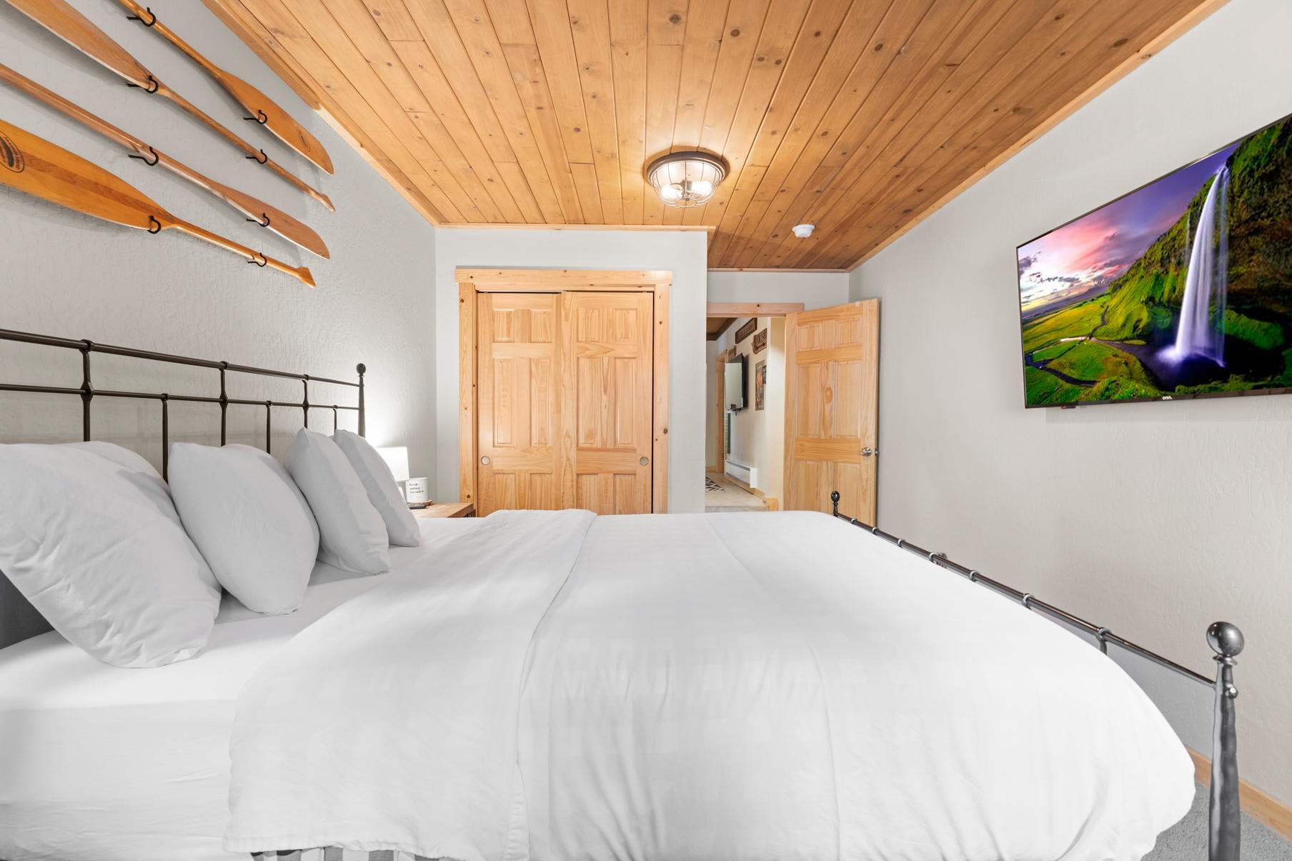 Cozy bedroom in a Truckee vacation rental with wooden decor, wall-mounted TV, and paddles displayed above the bed.